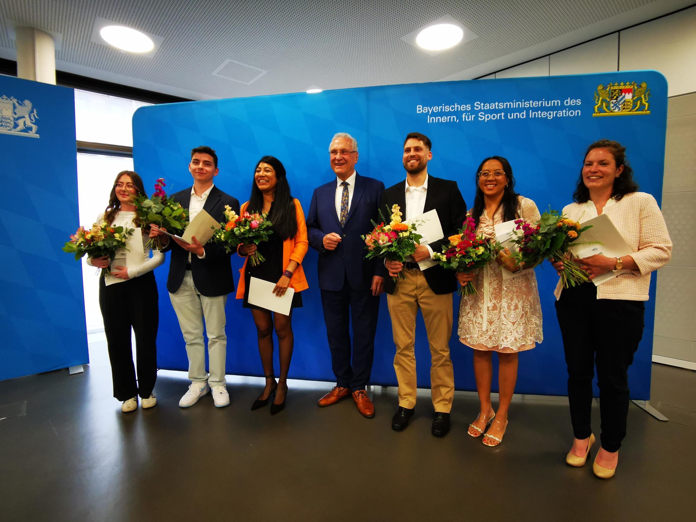 Frauen und Männer mit Blumensträußen und Einbürgerungsurkunden