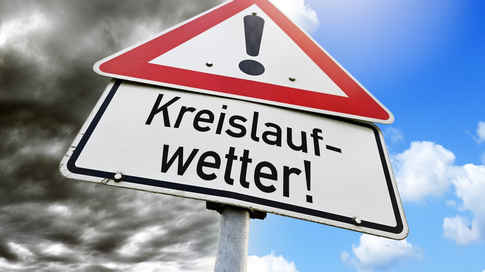 Ein Schild mit der Aufschrift "Kreislaufwetter" vor einem bewölktem und auf der anderen Bildseite strahlend blauem Himmel