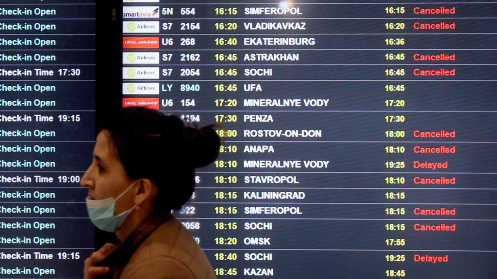 Eine Frau läuft an einer Anzeigetafel vorbei, auf der viele Flüge als "cancelled" aufgelistet sind.