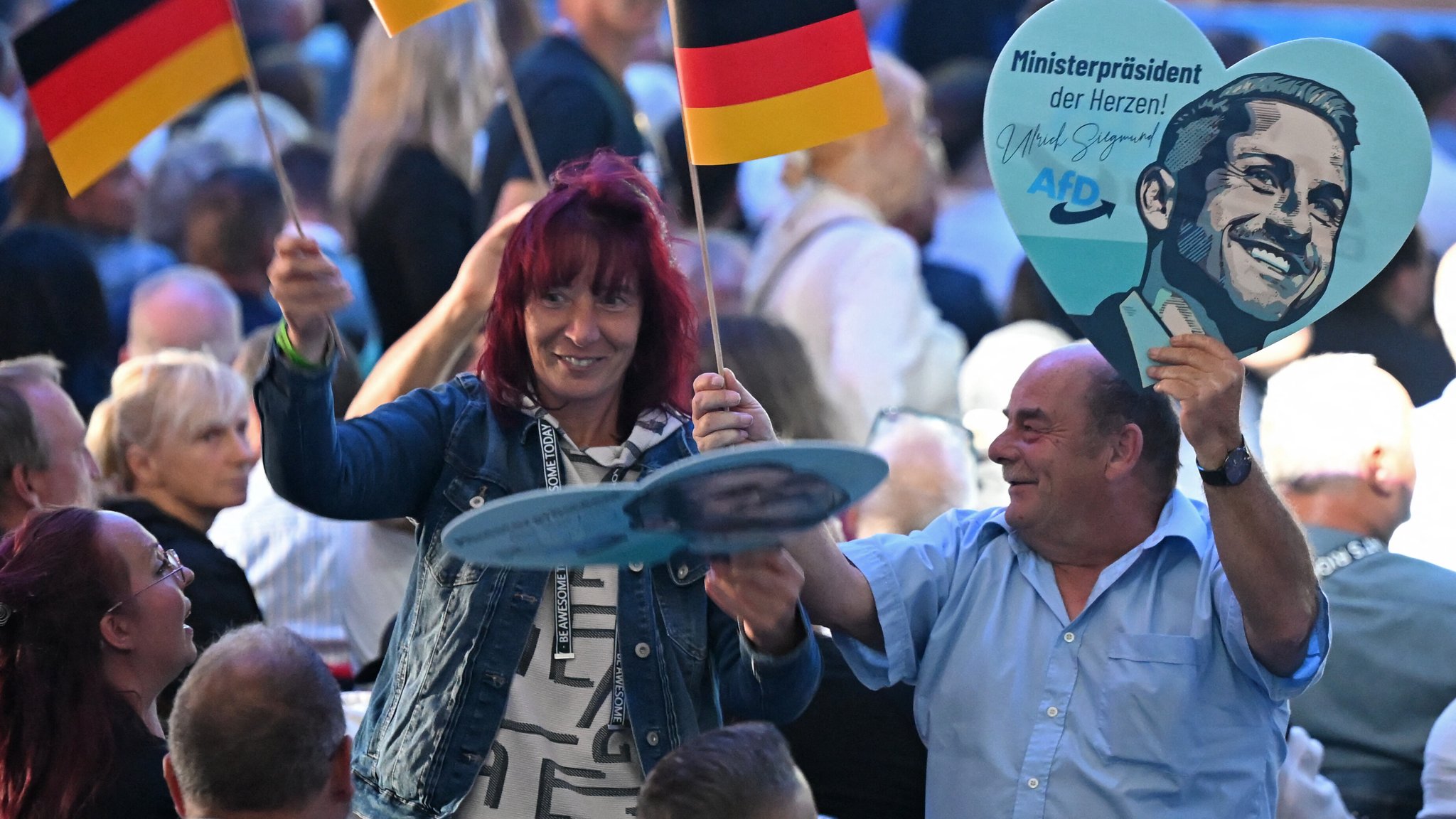 Zwei Teilnehmende schwenken Deutschlandflaggen und Poster für den Spitzenkandidaten Siegmund beim AfD-Wahlkampfabschluss in Magdeburg.