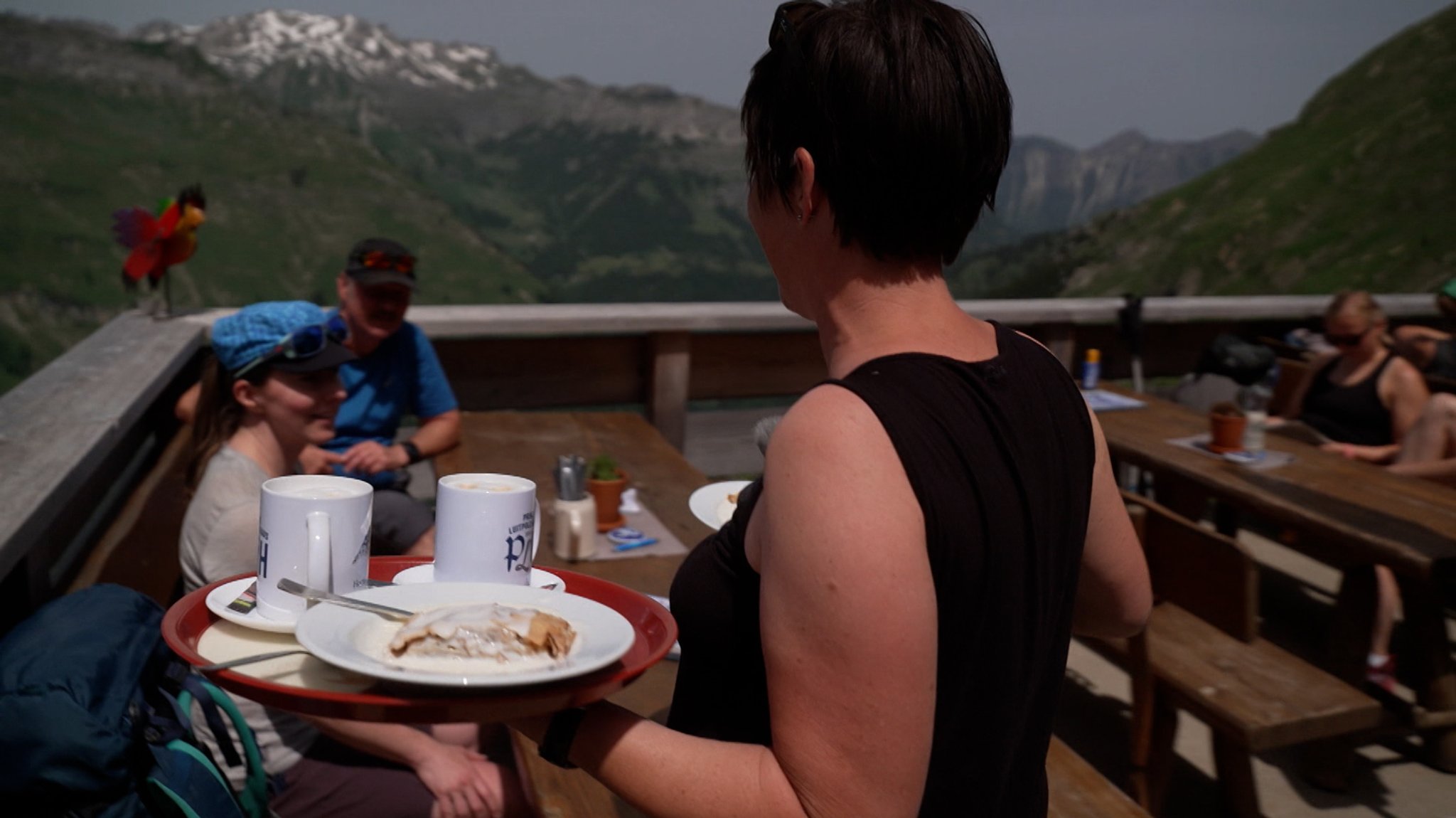 Eine Frau serviert auf der Terrasse des Prinz-Luitpold-Hauses einen Strudel mit Vanillesoße und zwei Haferl Kaffee