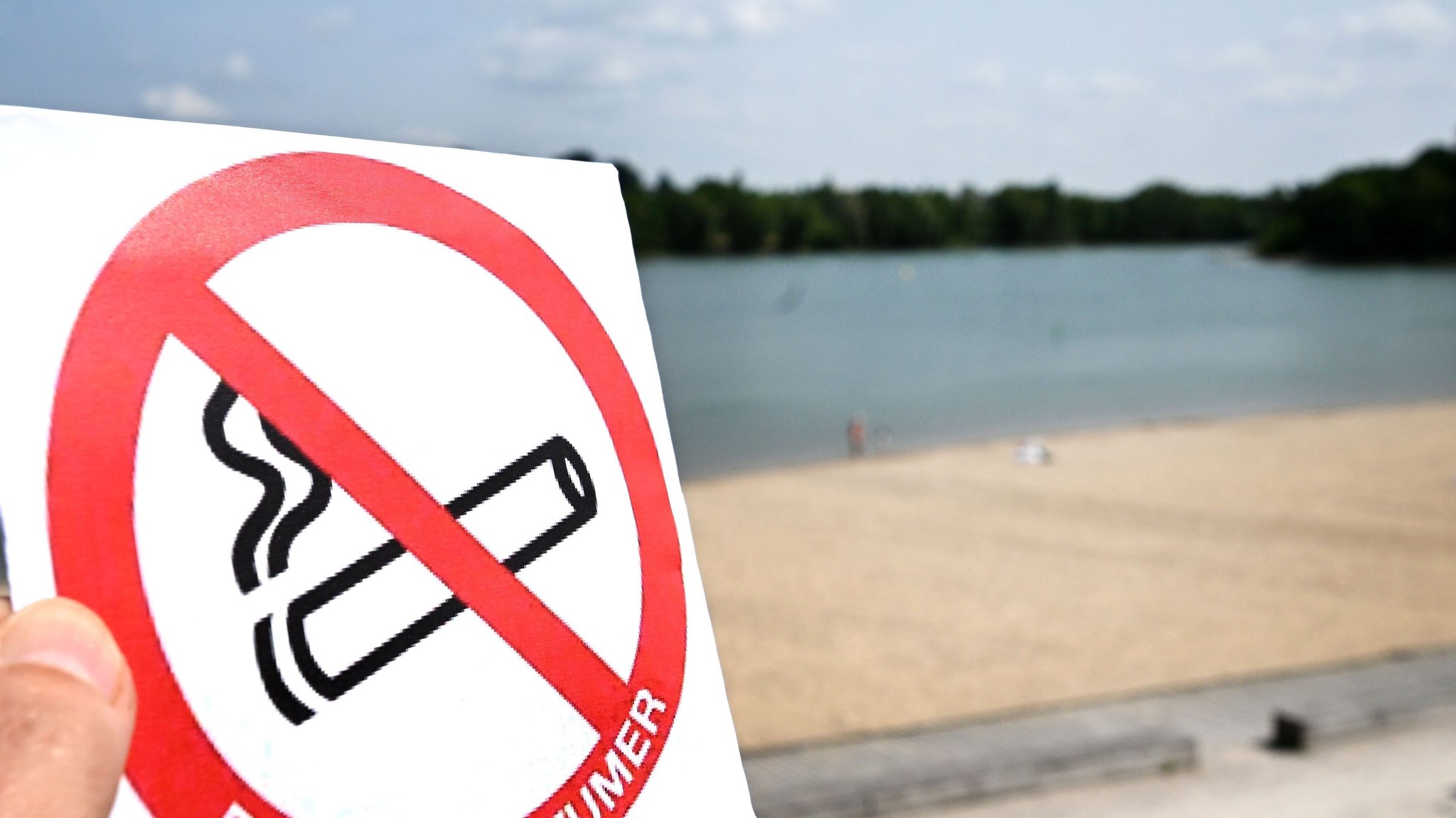 Eine Hand hält ein Rauchverbotsschild vor einem französischen Strand (Symbolbild)