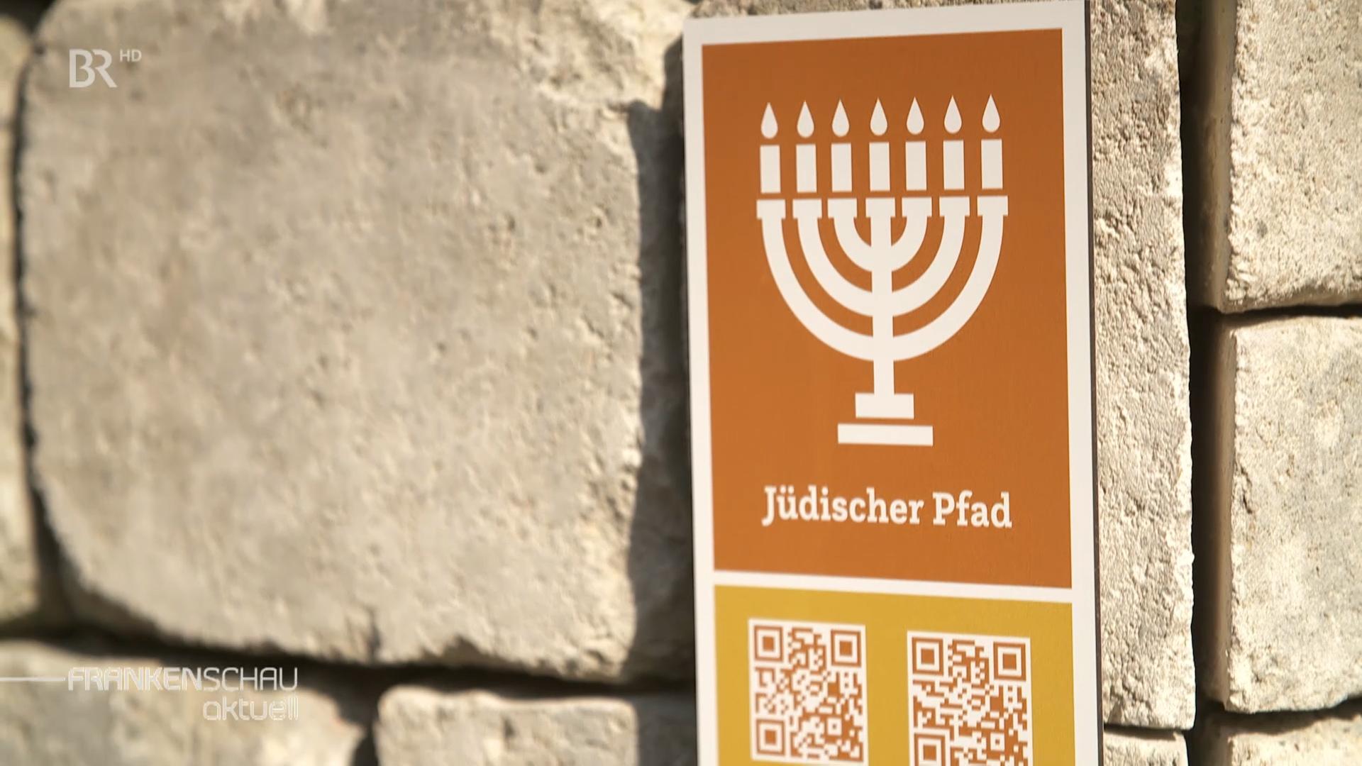 Ein Schild zeigt einen siebenarmigen Gebetsleuchter, darunter ist "Jüdischer Pfad" zu lesen. 