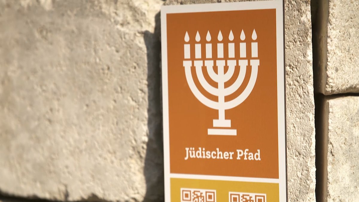 Ein Schild zeigt einen siebenarmigen Gebetsleuchter, darunter ist "Jüdischer Pfad" zu lesen. 