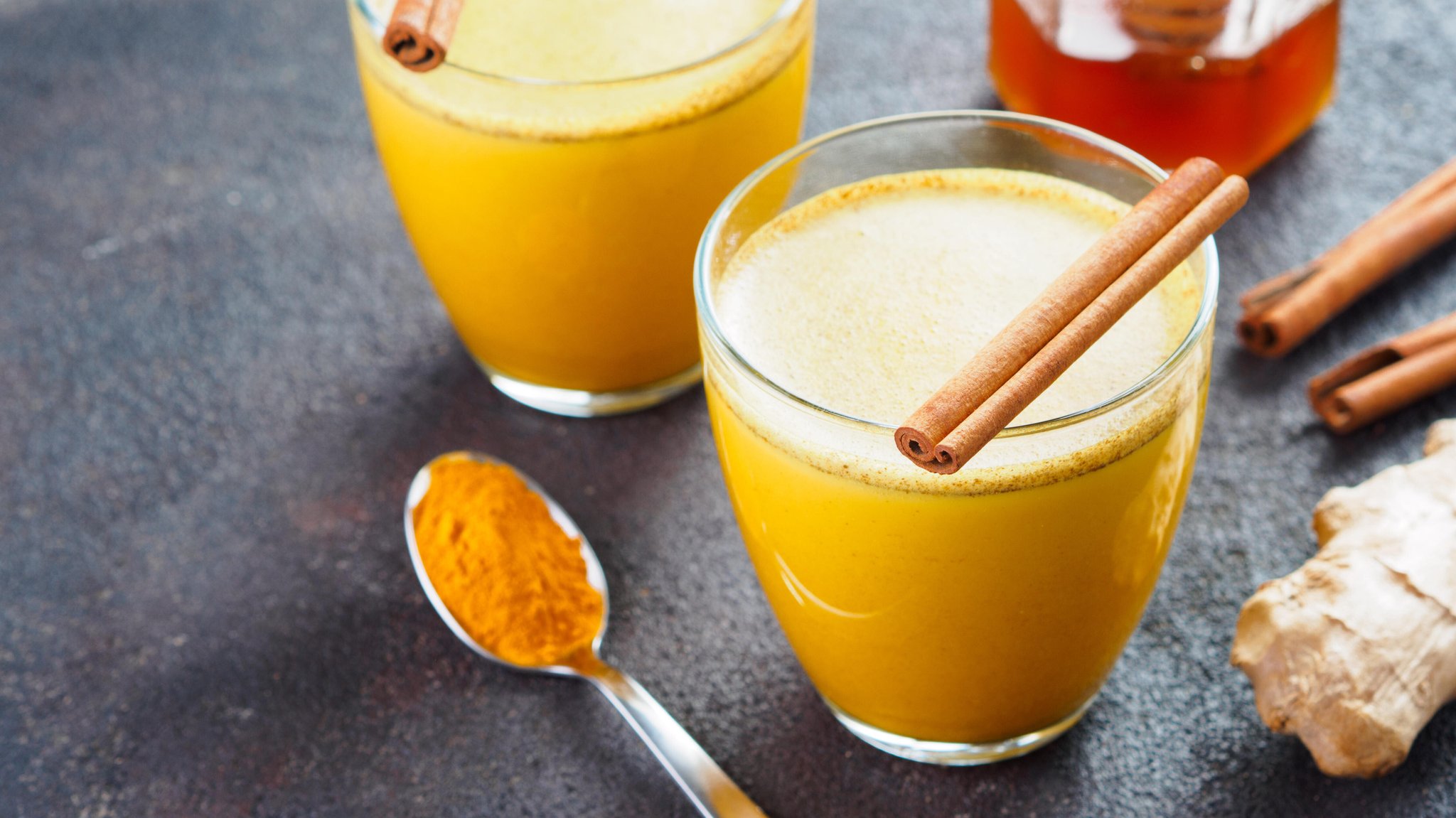 Ein Löffel mit Kurkumapulver, zwei Tassen mit "goldener Milch" 