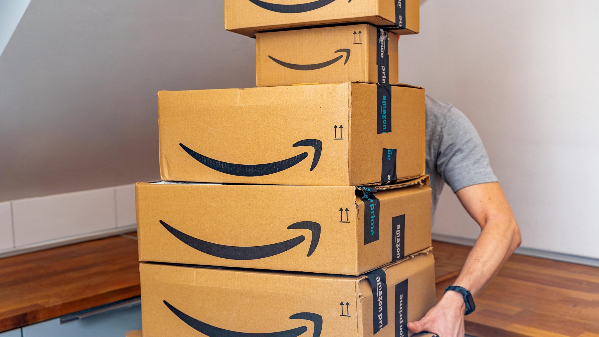 Mann trägt einen Stapel mit Amazon-Paketen