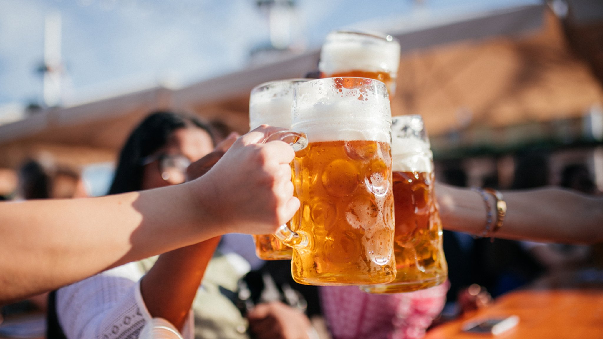 Vier Frauen stoßen in einem Biergarten auf der Wiesn zusammen mit einer Maß Bier an, die Frauen und das Oktoberfestzelt sind im Hintergrund in Unschärfe. Derzeit baut die Brauerei "Münchner Kindl" einen Tiefbrunnen im Stadtgebiet und schafft damit die Voraussetzung, "Münchner Bier" brauen zu können - als achte Brauerei. (Symbolbild)