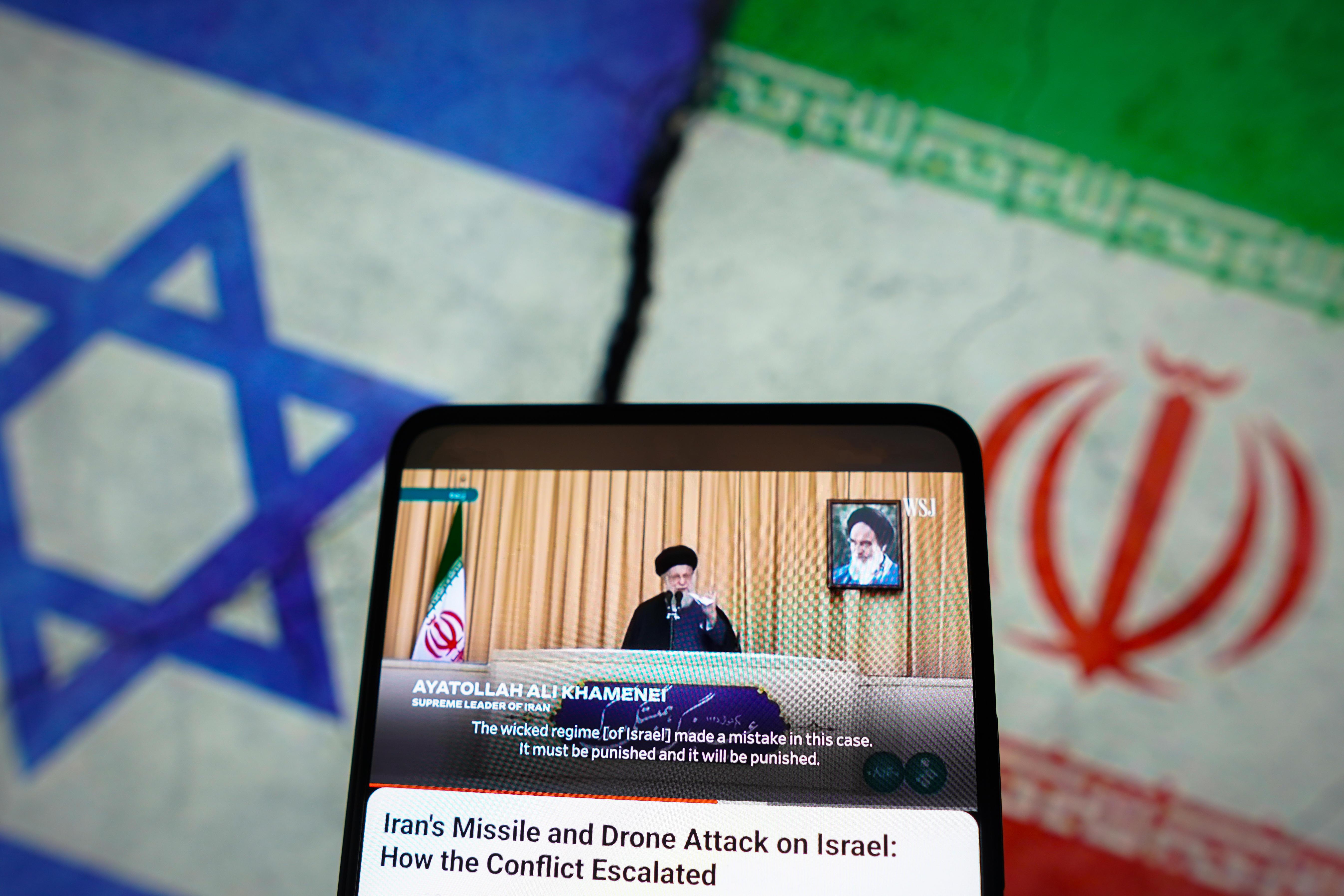 Collage: Israel und Iran-Flagge, davor ein Handy mit aktuellen News über eine Rede von Irans Revolutionsführer Ayatollah Ali Chamenei.