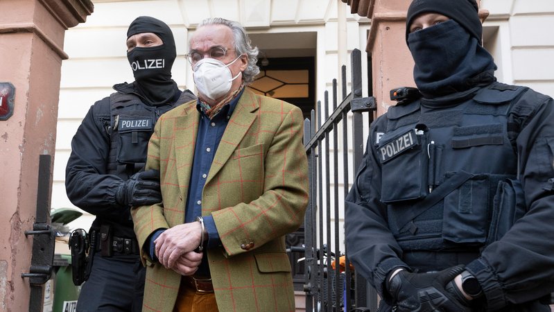 Bei einer Razzia gegen sogenannte "Reichsbürger" führen vermummte Polizisten Heinrich XIII. Prinz Reuß im Dezember 2022 zu einem Polizeifahrzeug. | Bild: picture alliance/dpa | Boris Roessler Bei einer Razzia gegen sogenannte "Reichsbürger" führen vermummte Polizisten Heinrich XIII. Prinz Reuß im Dezember 2022 zu einem Polizeifahrzeug.
