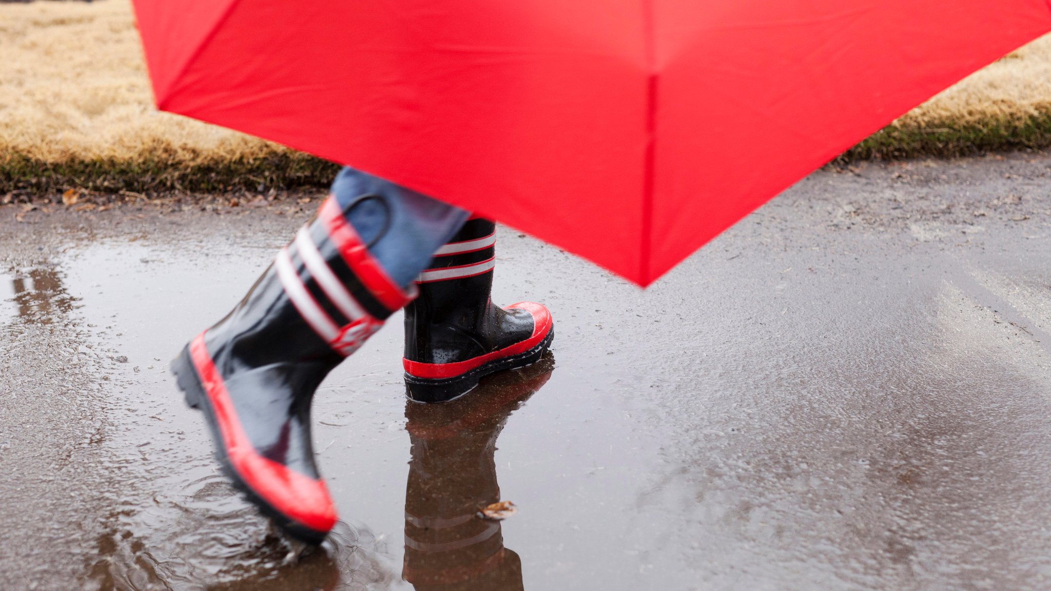 Ein Kind geht mit Gummistiefeln und Schirm durch den Regen 