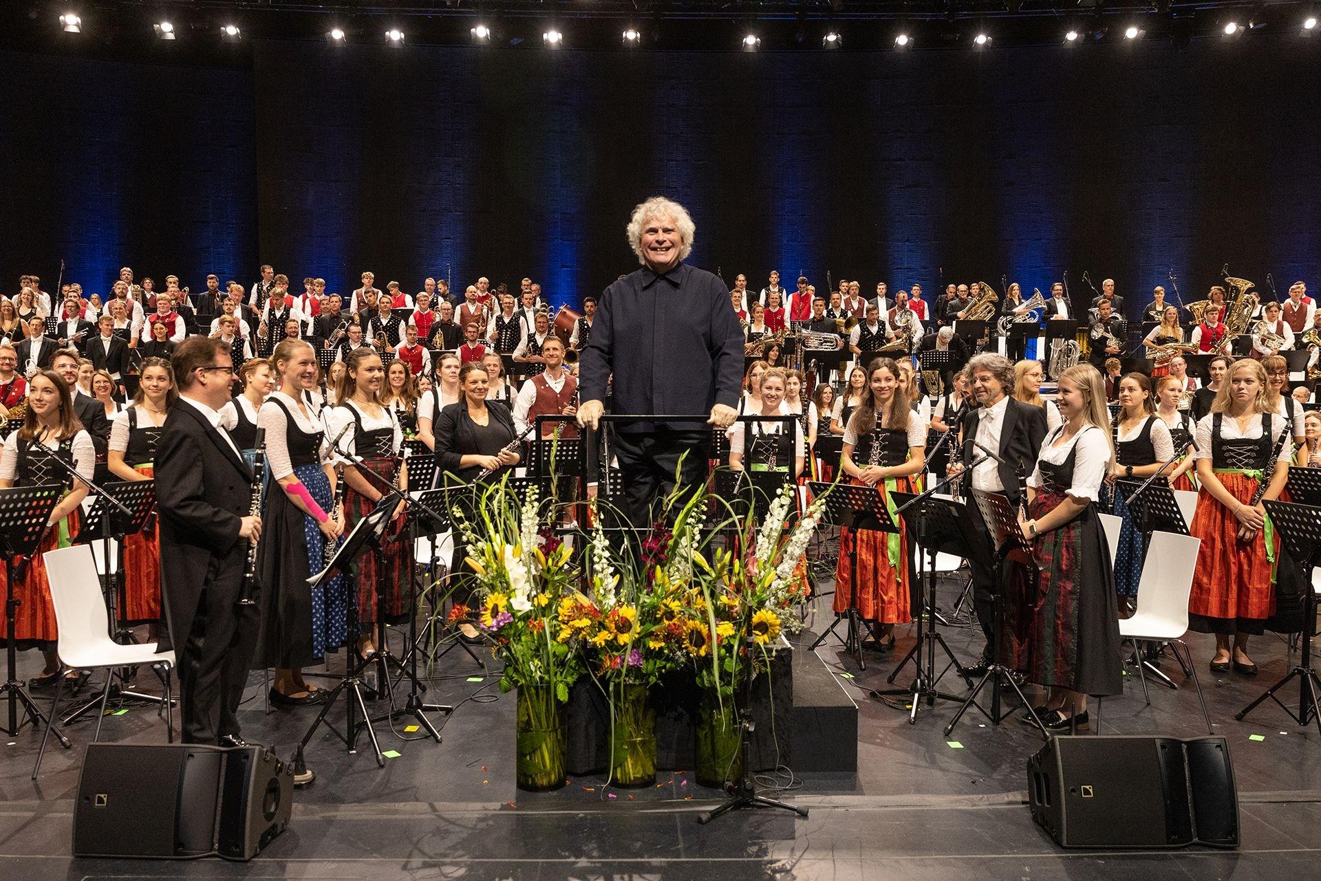 Auf dem Dirigentenpult steht Sir Simon Rattle - vor 300 Musikern aus vier Blaskapellen und dem Bayerischen Symphonieorchester.