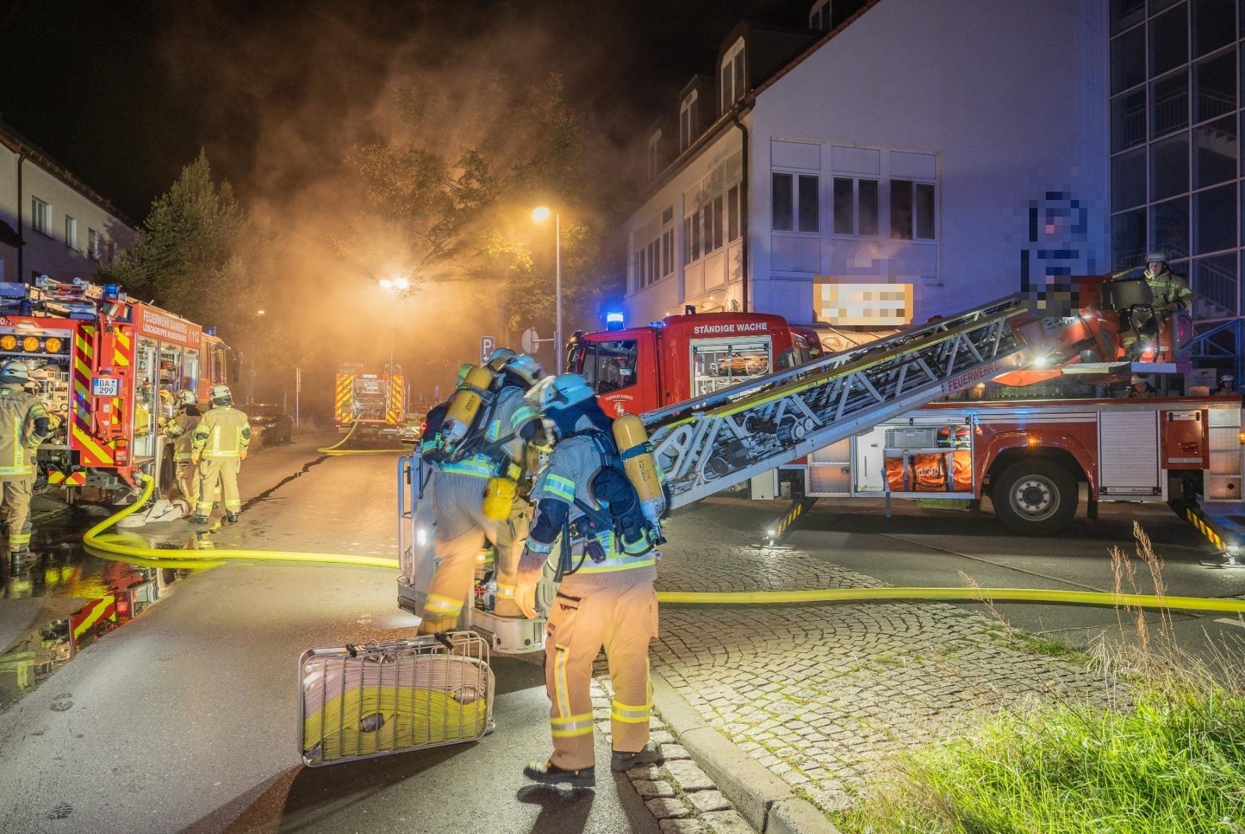 Feuerwehrleute stehen vor einem Hotel in Bamberg Die Straße ist verraucht. 