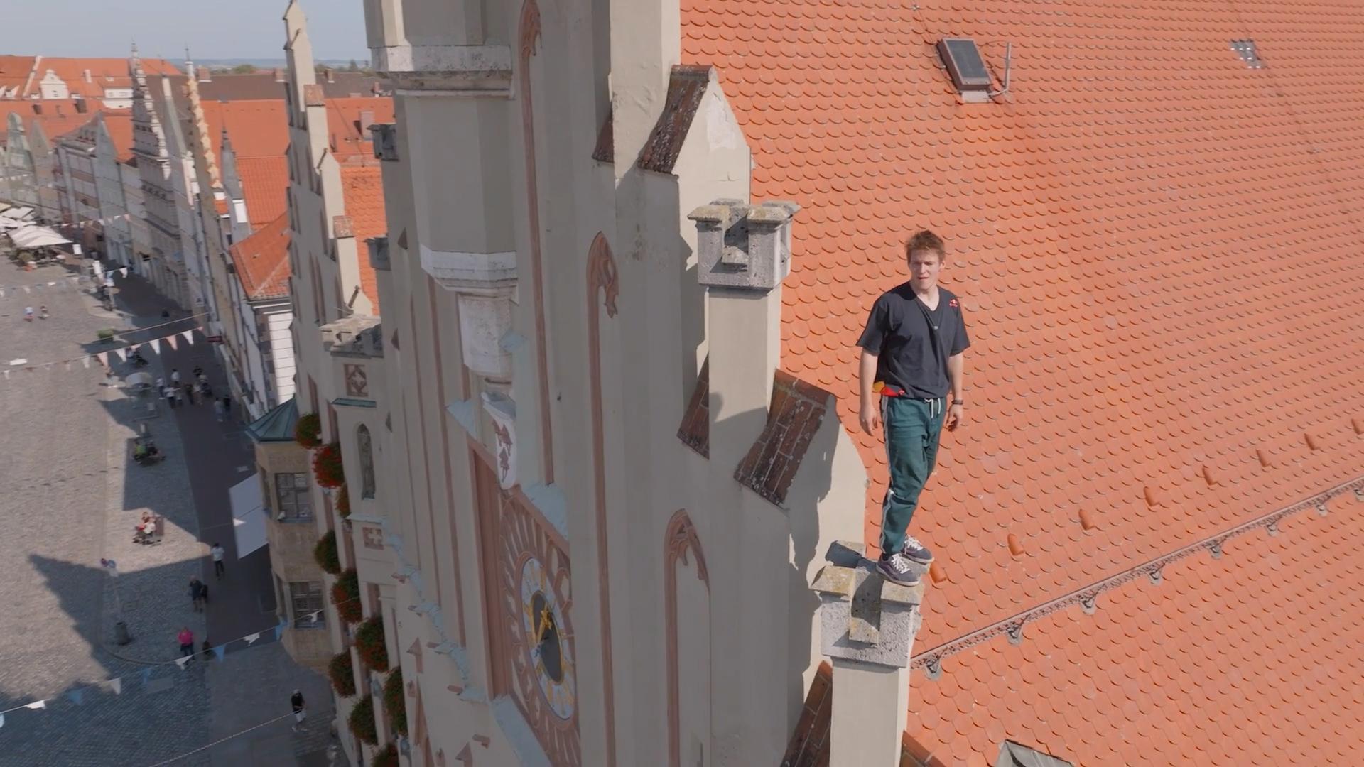 Ein Mann steht hoch oben auf dem Giebel eines Hauses in der Landshuter Altstadt. 