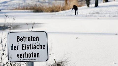 Vor einem zugefrorenen See steht ein Schild mit der Aufschrift "Betreten der Eisfläche verboten".
