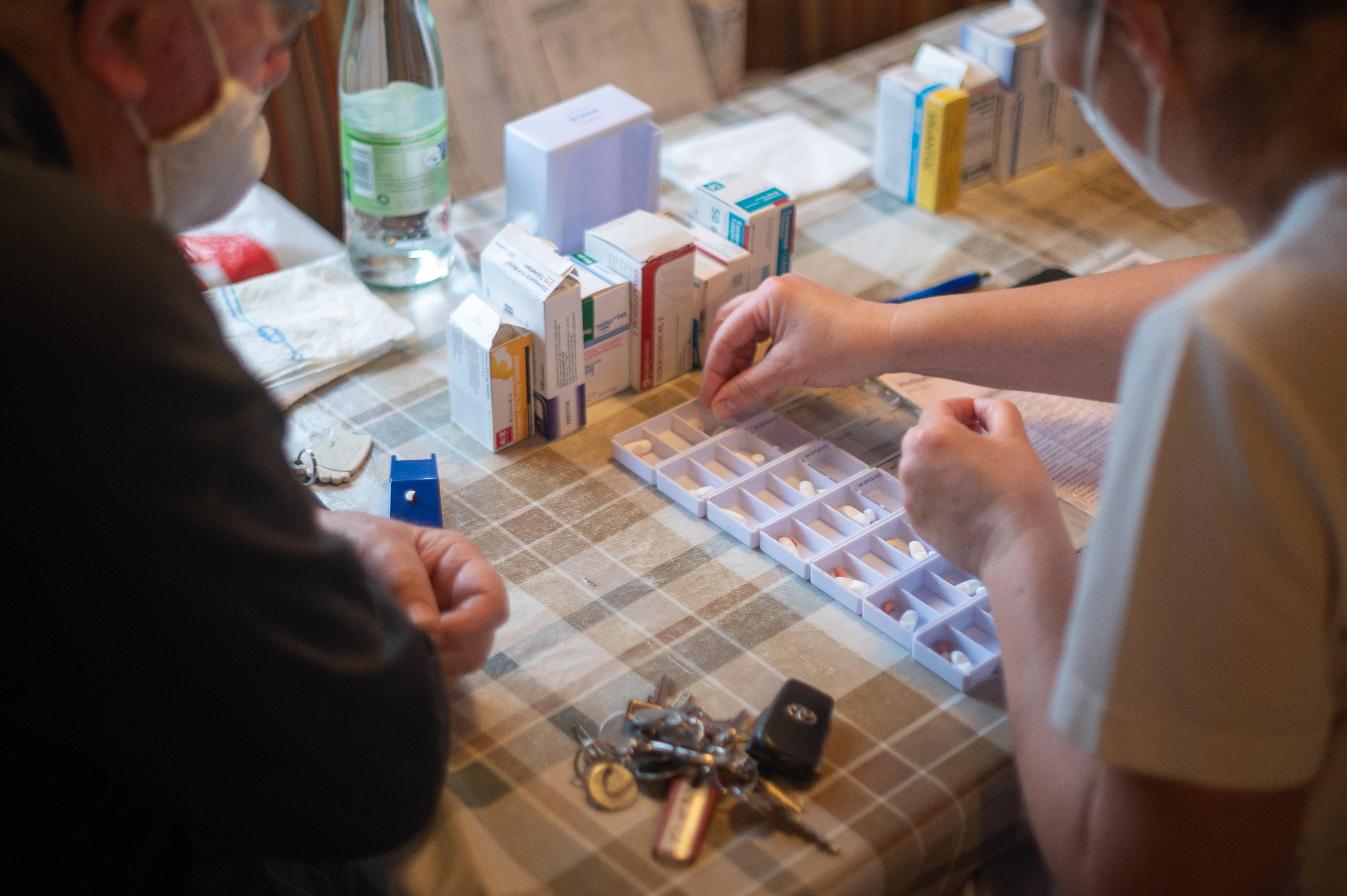 Eine Pflegefachkraft füllt während ihrer Schicht in der ambulanten Pflege neben einem Klienten Medikamente in Schalen (Symbolbild).
