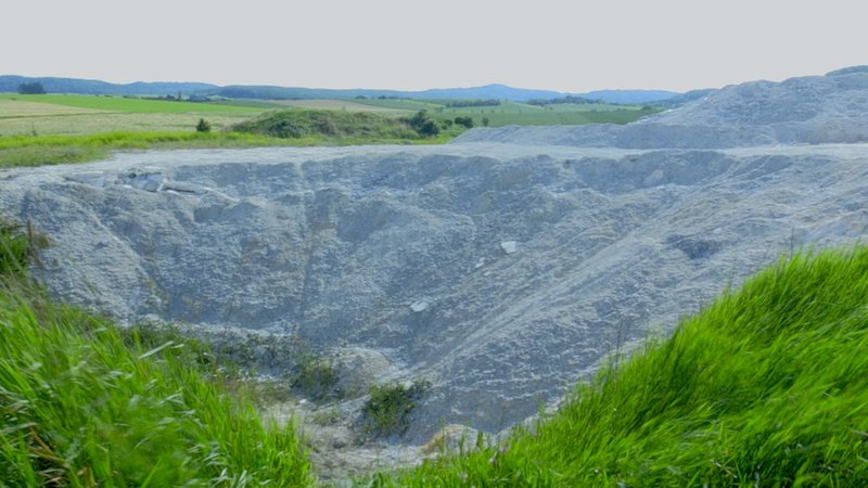 In einer Wiese befindet sich eine grauweiße Grube. | Bild: BR24/Laura Nadler In einer Wiese befindet sich eine grauweiße Grube.