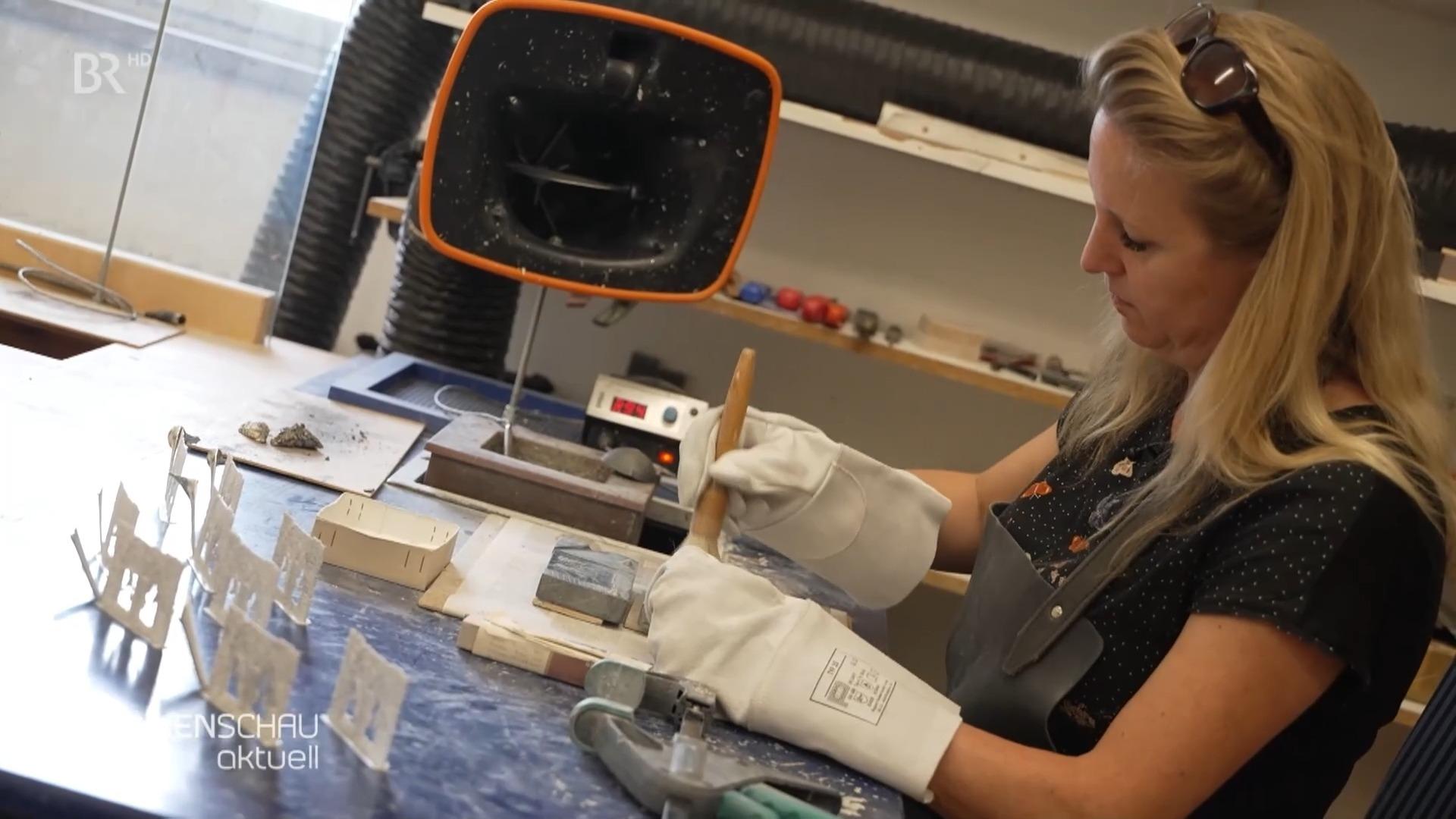 Eine Frau mit Handschuhen bearbeitet Zinnblöcke