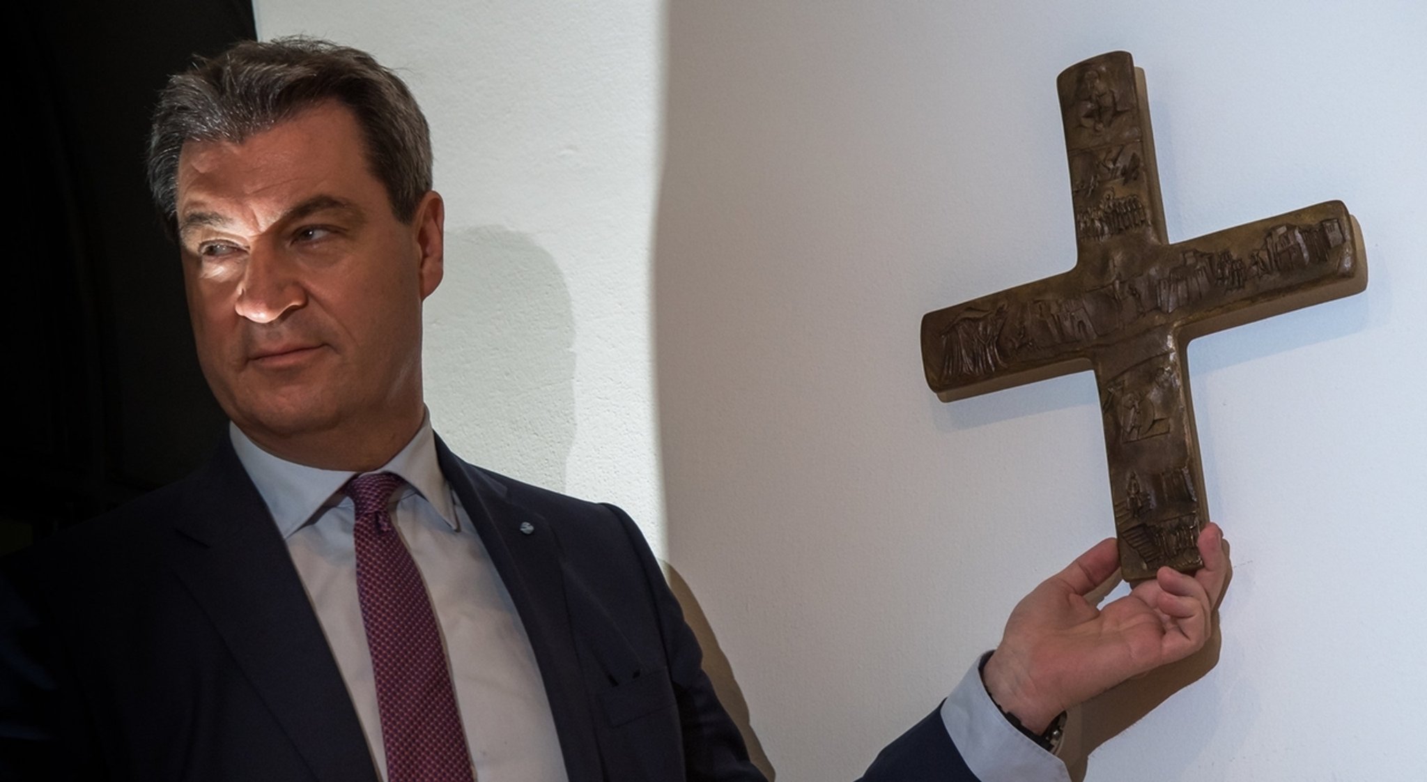 ARCHIV - 24.04.2018, Bayern, München: Markus Söder, Bayerischer Ministerpräsident (CSU), hängt ein Kreuz im Eingangsbereich der bayerischen Staatskanzlei auf. Der umstrittene Kreuzerlass der Staatsregierung wird ein Fall für den Bayerischen Verwaltungsgerichtshof. Foto: Peter Kneffel/dpa +++ dpa-Bildfunk +++