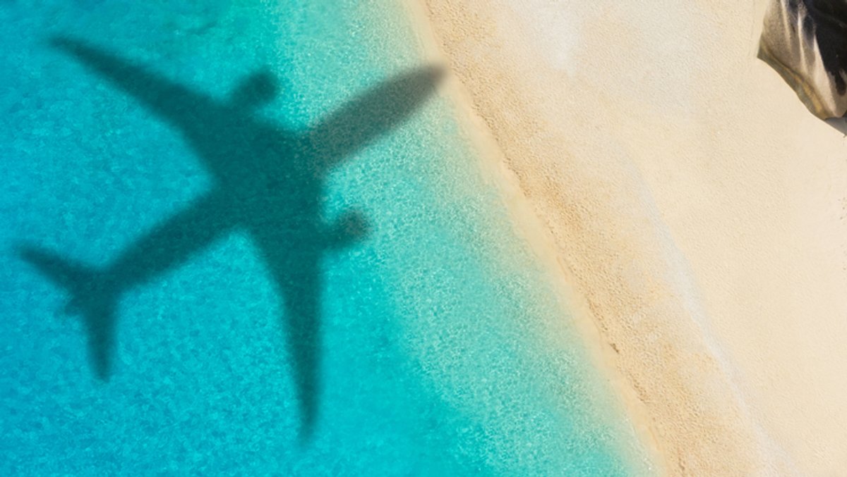 Der Schatten eines Flugzeuges über einem paradiesischem Sandstrand und türkisblauem Meer.