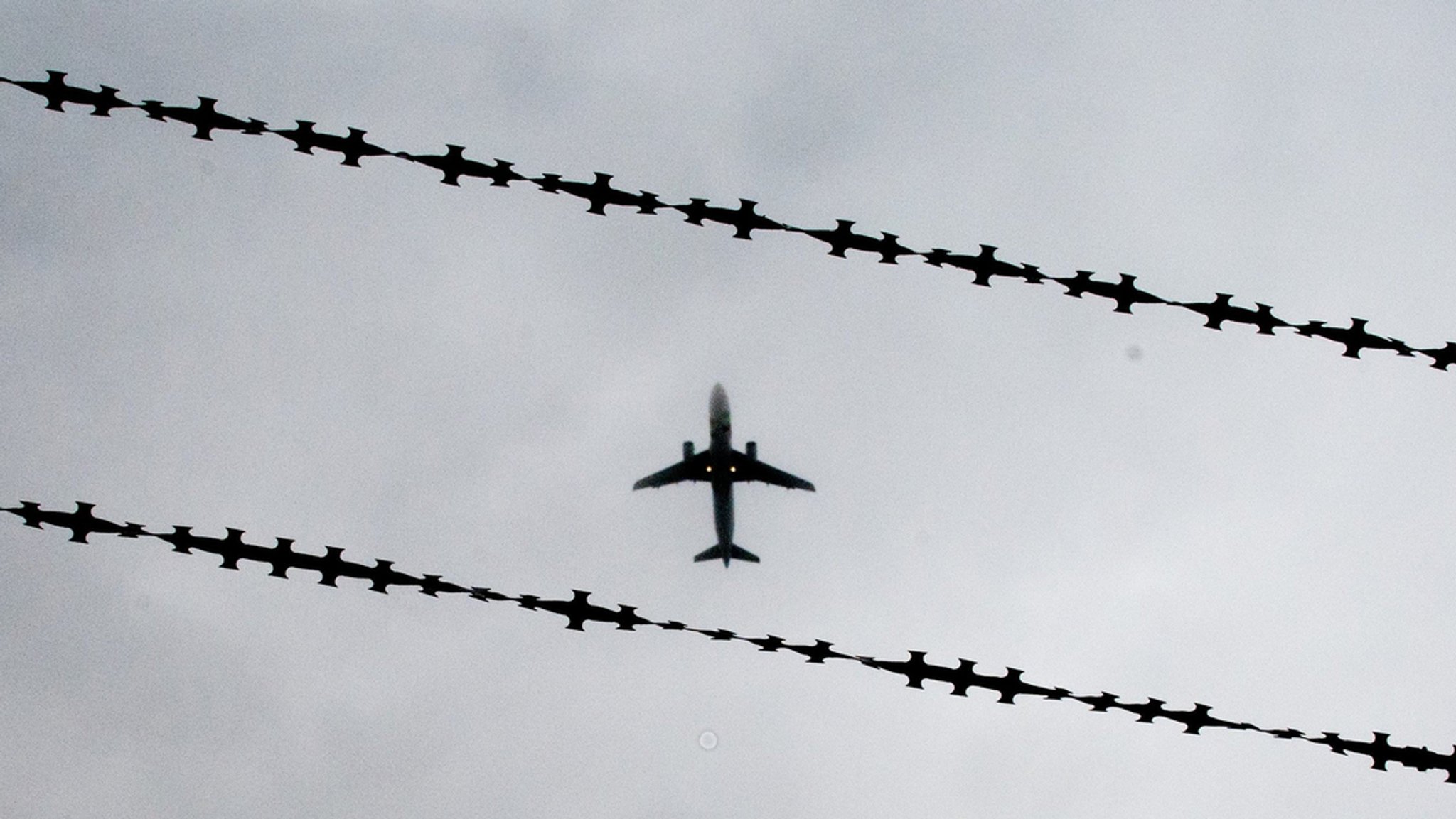 Ein Flugzeug im Himmel - hinter einem Stacheldrahtzaun