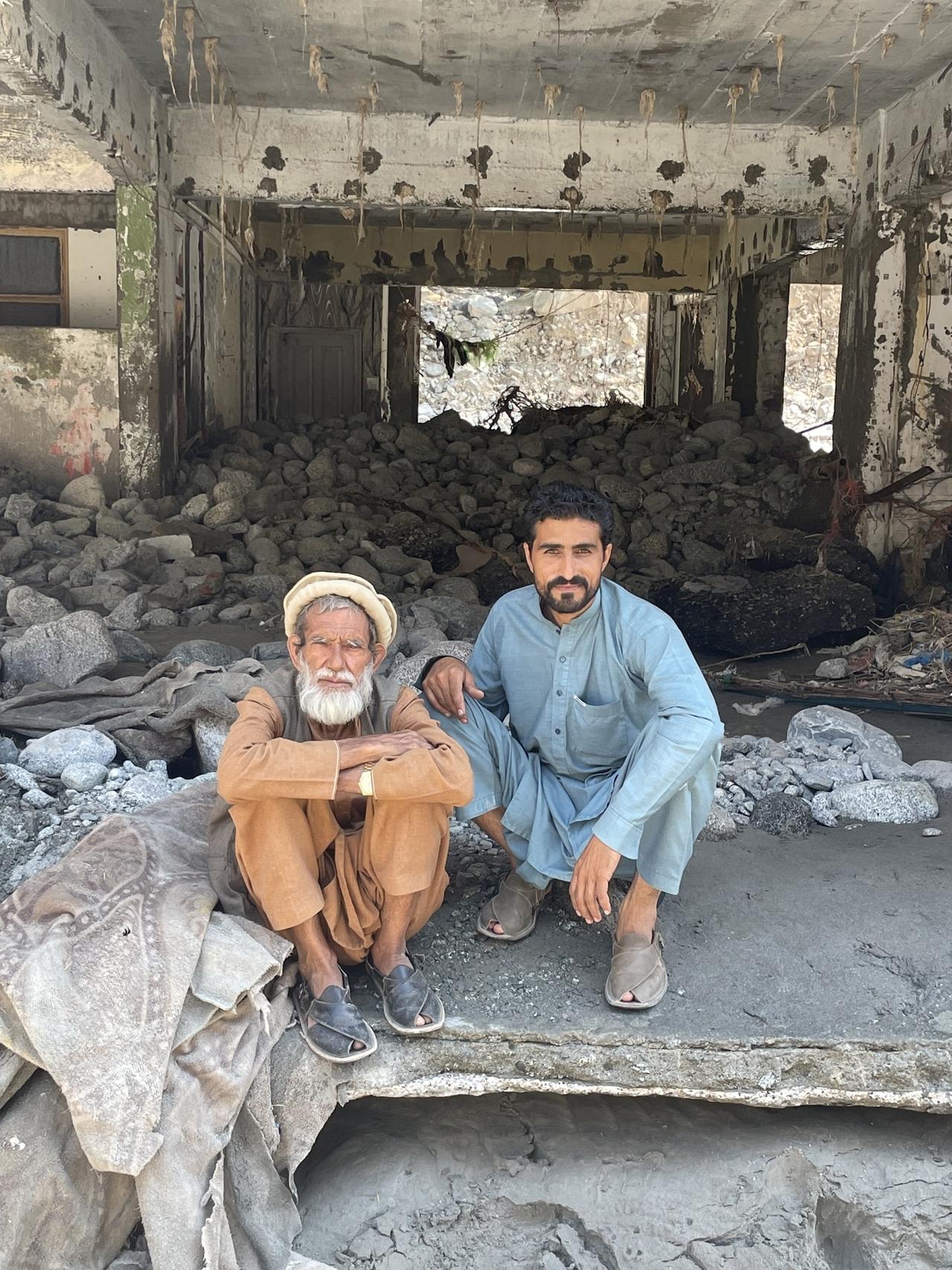 Ein alter Mann und ein junger Mann sitzen auf der Schwelle eines von der Flut zerstörten Hauses.