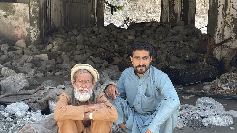Ein alter Mann und ein junger Mann sitzen auf der Schwelle eines von der Flut zerstörten Hauses.