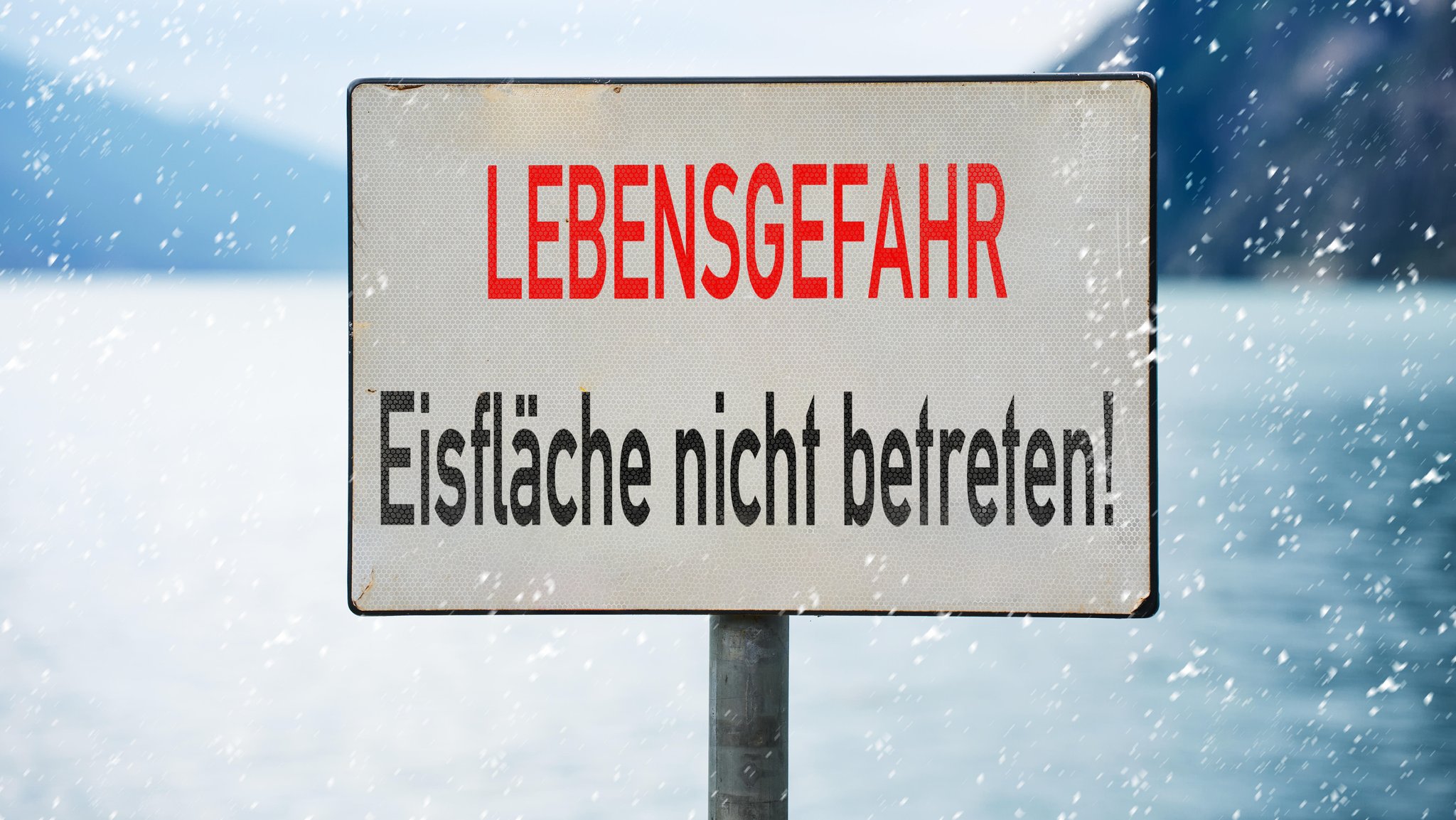 Ein Schild mit der Aufschrift: "Lebensgefahr: Eisfläche nicht betreten" vor winterlicher Kulisse