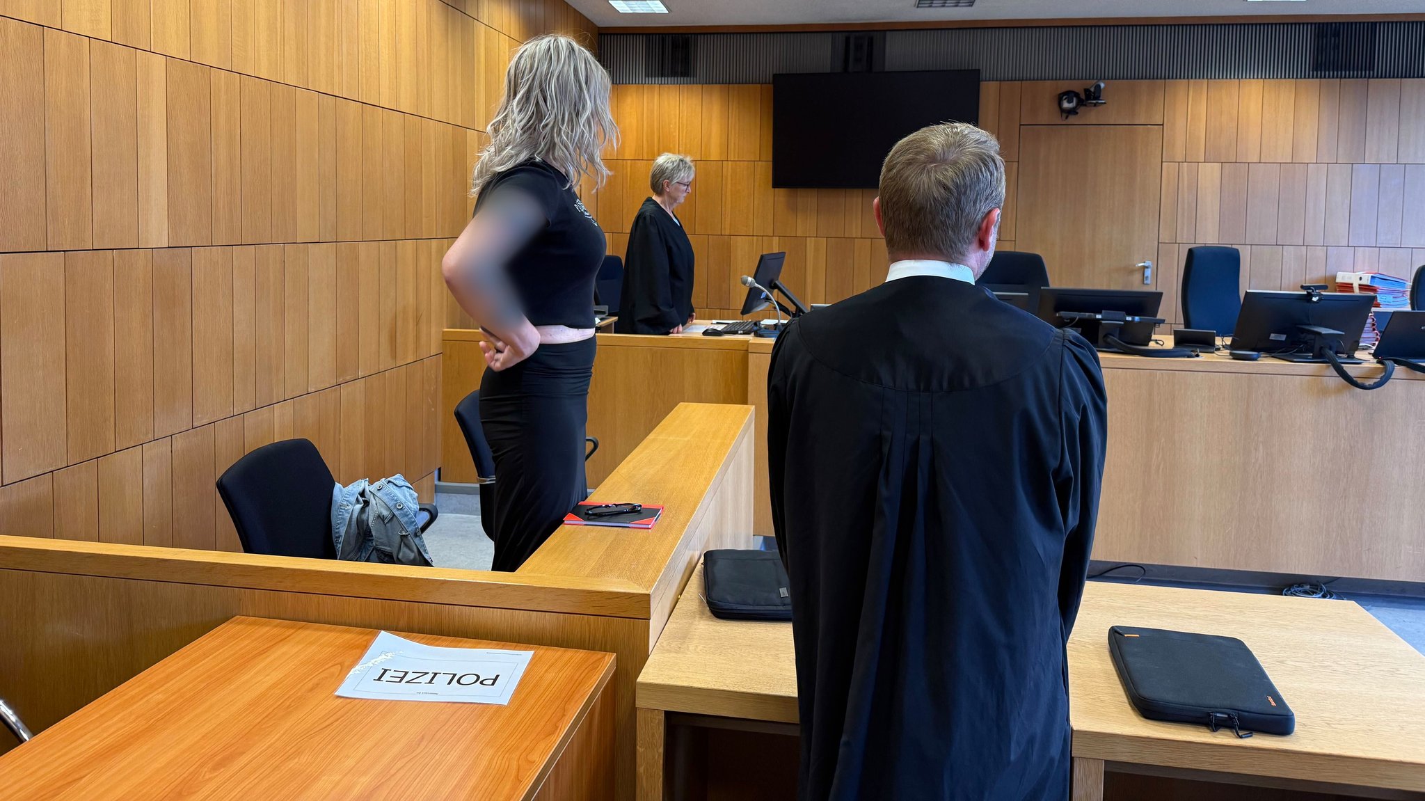 Zu sehen ist die Angeklagte im Verhandlungssaal des Landgerichts Traunstein. Ein Anwalt kehrt der Kamera den Rücken zu. 