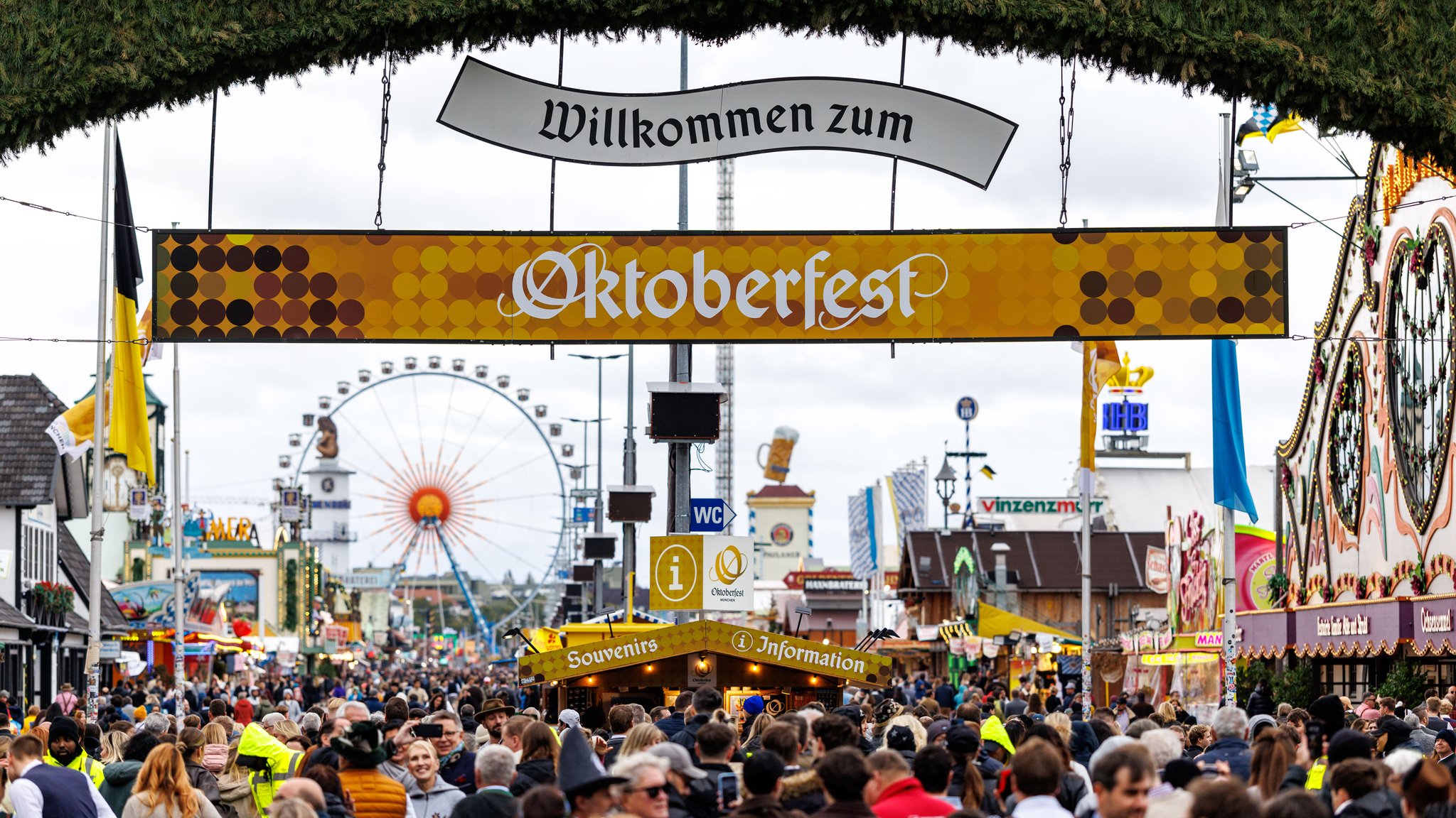 ARCHIV (05.10.2025). Symbolbild eingang Oktoberfest. Zahlreiche Besucher gehen am 05.10.2025 am frühen Morgen kurz nach der ffnung durch das Tor vom Haupteingang auf das 190. Oktoberfest auf der Theresienwiese in München (Bayern, Deutschland), während im Hintergrund die Bierzelte (Festzelte) der Brauereien und das Riesenrad zu sehen sind. 