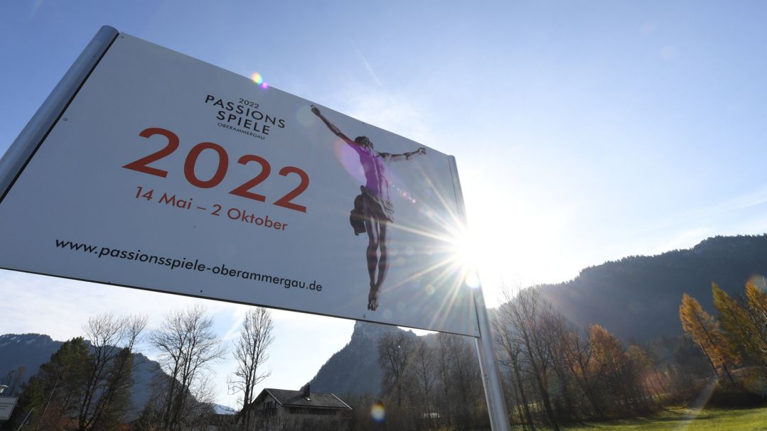 Die Sonne blickt hinter einem Plakat für die Passionsspiele 2022 hervor.