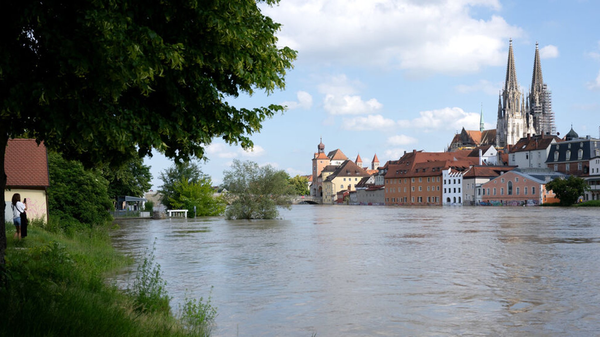 04.06.2024, Bayern, Regensburg: Ein Frau (l) fotografiert in der Altstadt am Donauufer das Hochwasser. Seit Tagen kämpfen die Helfer in Bayern gegen die Flut und ihre Folgen. Foto: Sven Hoppe/dpa +++ dpa-Bildfunk +++