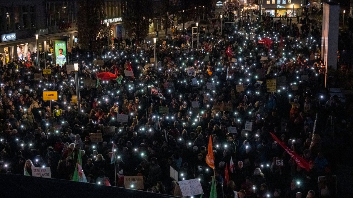Demonstrantinnen und Demonstranten halten in Nürnberg ihre leuchtenden Handys in die Luft. 
