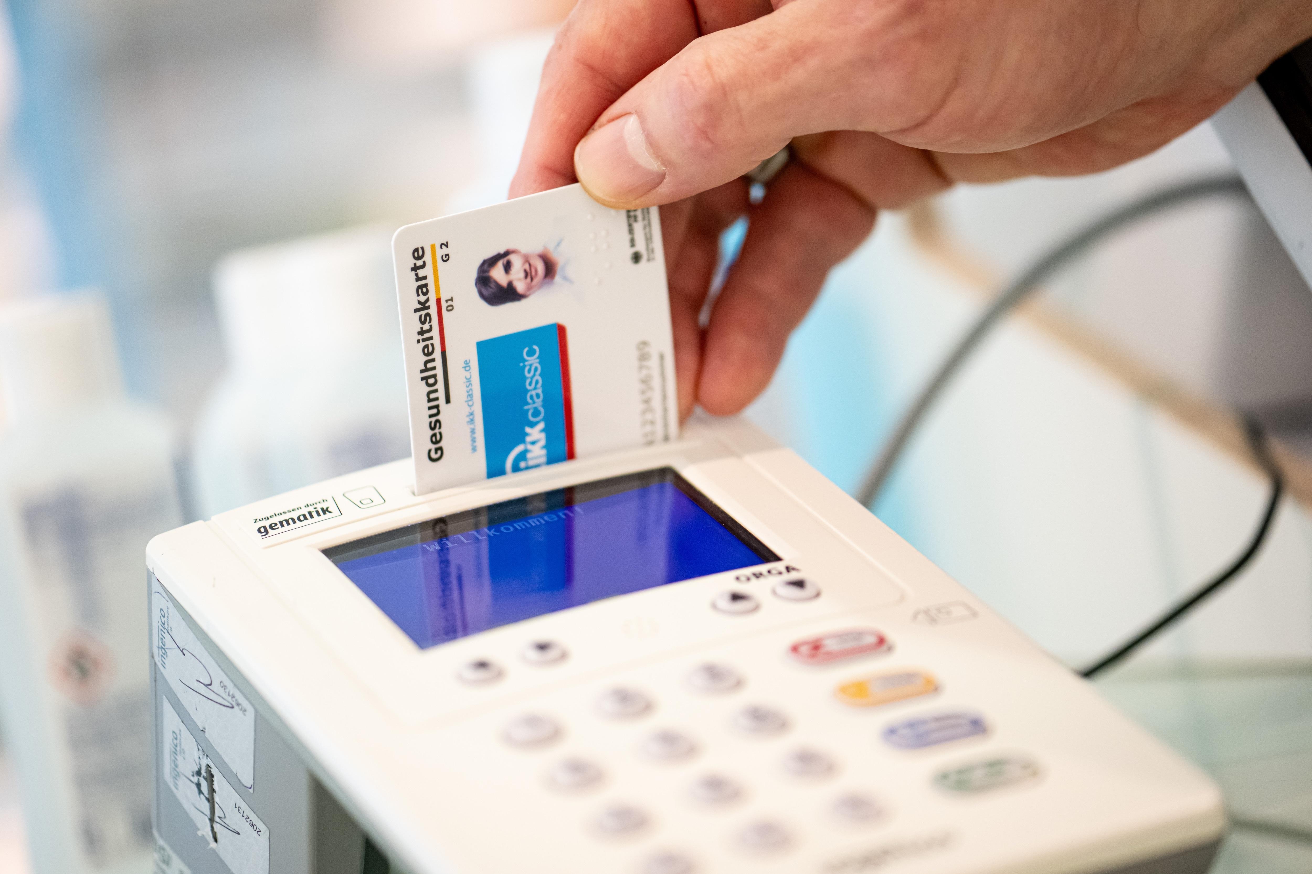 Ein Mitarbeiter einer Apotheke steckt eine Gesundheitskarte in ein Lesegerät.