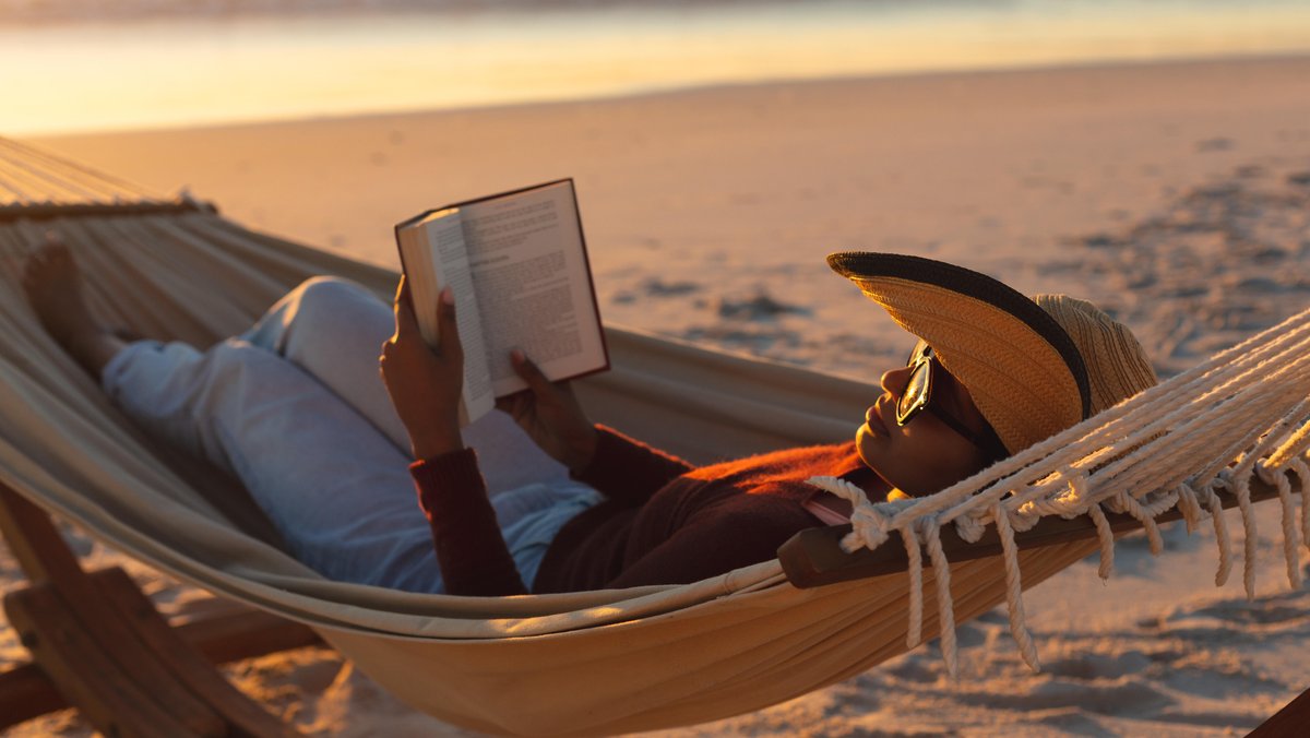 Eine Frau liegt bei untergehender Sonne mit in einer Hängematte und liest