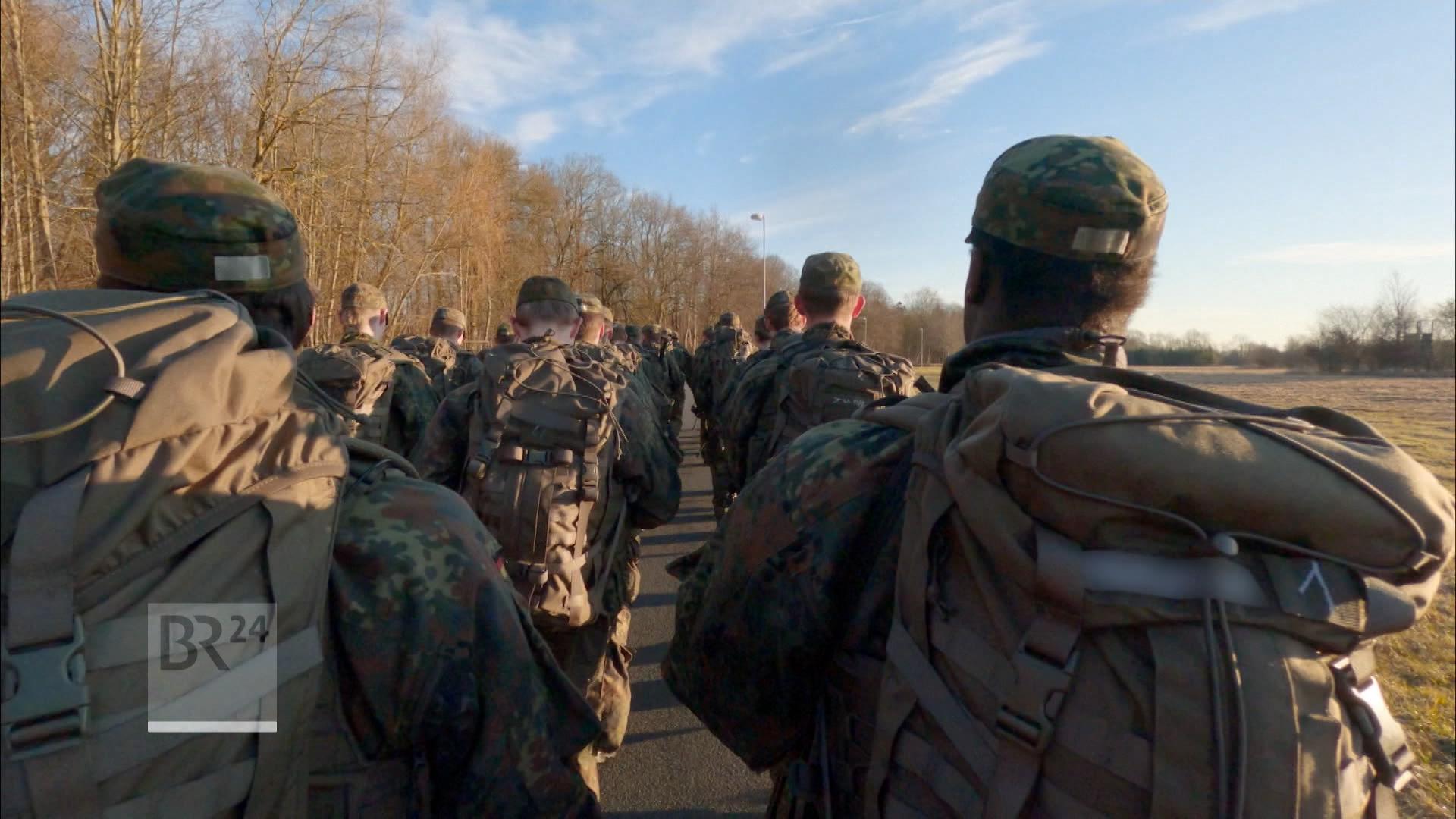 Soldaten marschieren mit Rucksäcken auf einem Feldweg