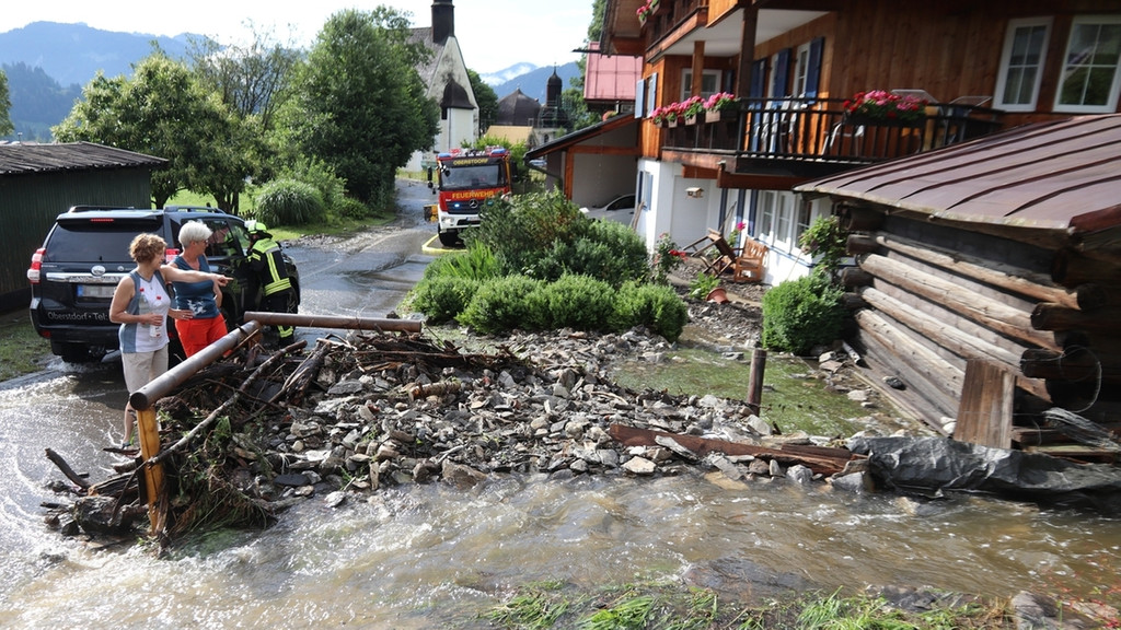 Anwohner betrachten die Schäden durch starke Regenfälle. Starkregen hat am Donnerstag zahlreiche Straßen im südlichen Allgäu überflutet. 