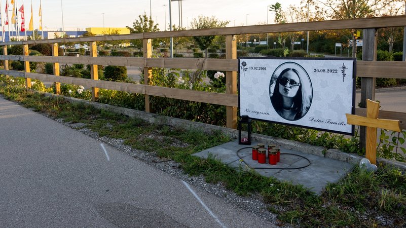 Am Rand des Parkplatzes eines Möbelhauses erinnern ein Plakat, ein Kreuz und Kerzen an die Frau, die bei dem Unfall in Augsburg gestorben ist