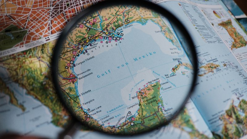 Eine Lupe wird in einem Atlas über den Golf von Mexiko gehalten (Illustration). | Bild: picture alliance / Jörg Carstensen | Joerg Carstensen Eine Lupe wird in einem Atlas über den Golf von Mexiko gehalten (Illustration).