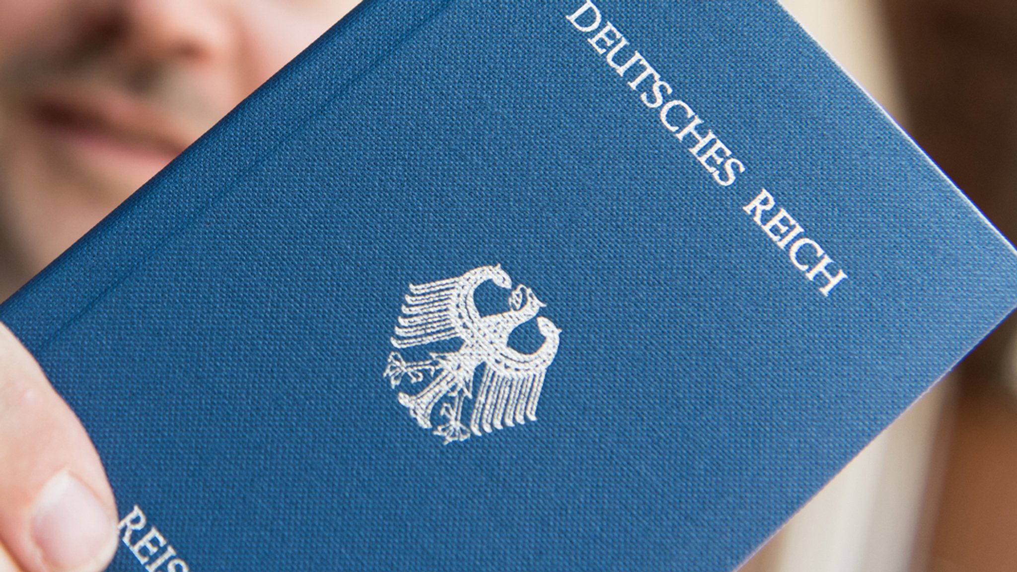 Eine Hand hält einen blauen Reisepass mit der Aufschrift "Deutsches Reich"