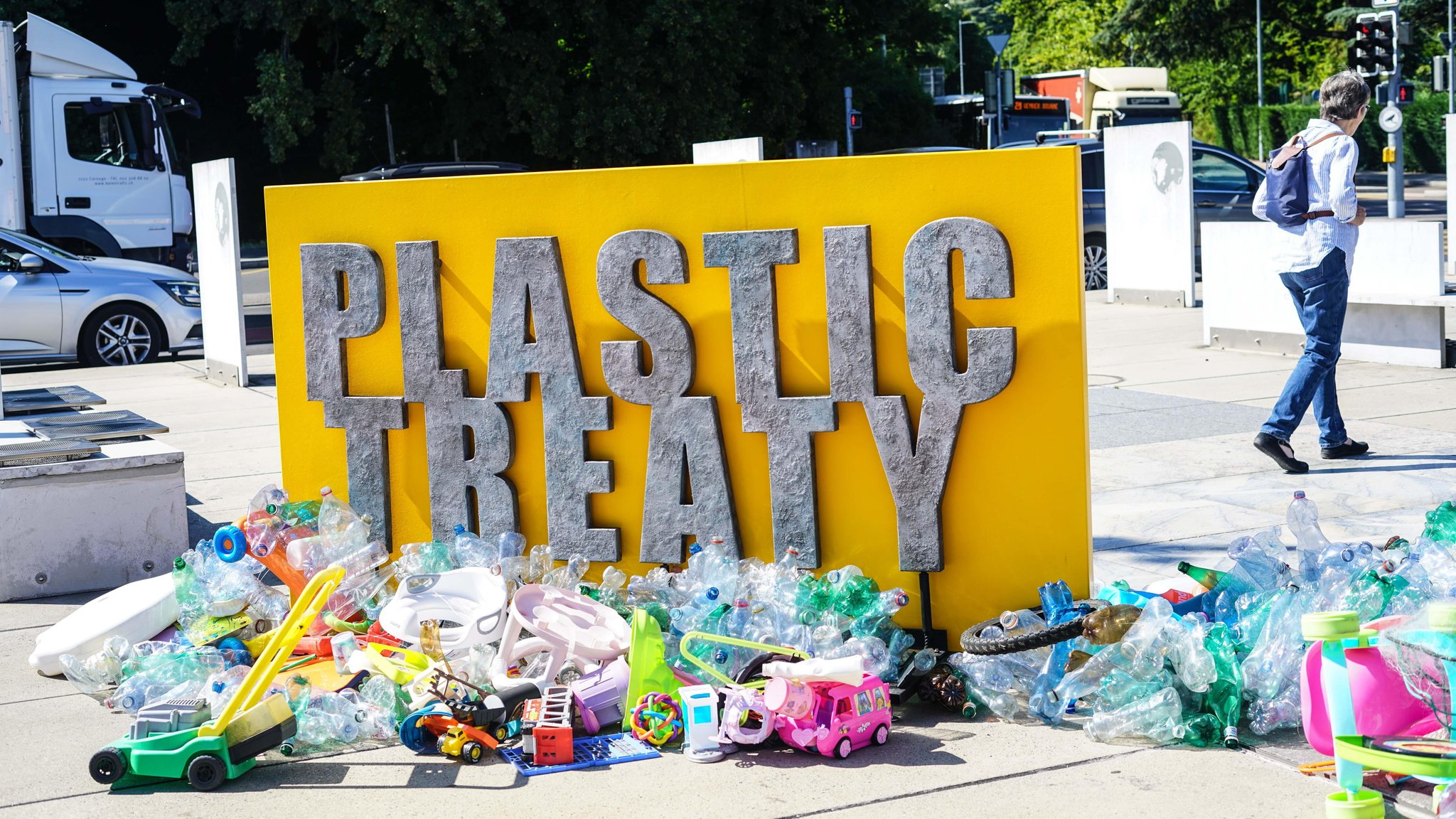 (Symbolbild) Kunstinstallation in Genf: Auf einer gelben Wand steht in großen grauen Buchstaben "Plastic Treaty". Am Boden davor liegt eine Menge Plastikmüll. 