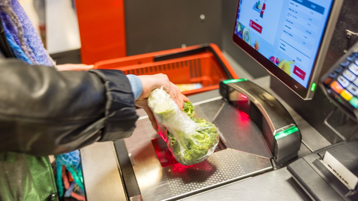 Eine Kundin führt verpackten Brokkoli über einen Scanner an einer Selbstbedienungskasse in einem Lebensmittelsupermarkt.