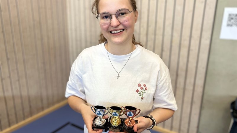 Eine junge Frau hält drei kleine Pokale in der Hand.