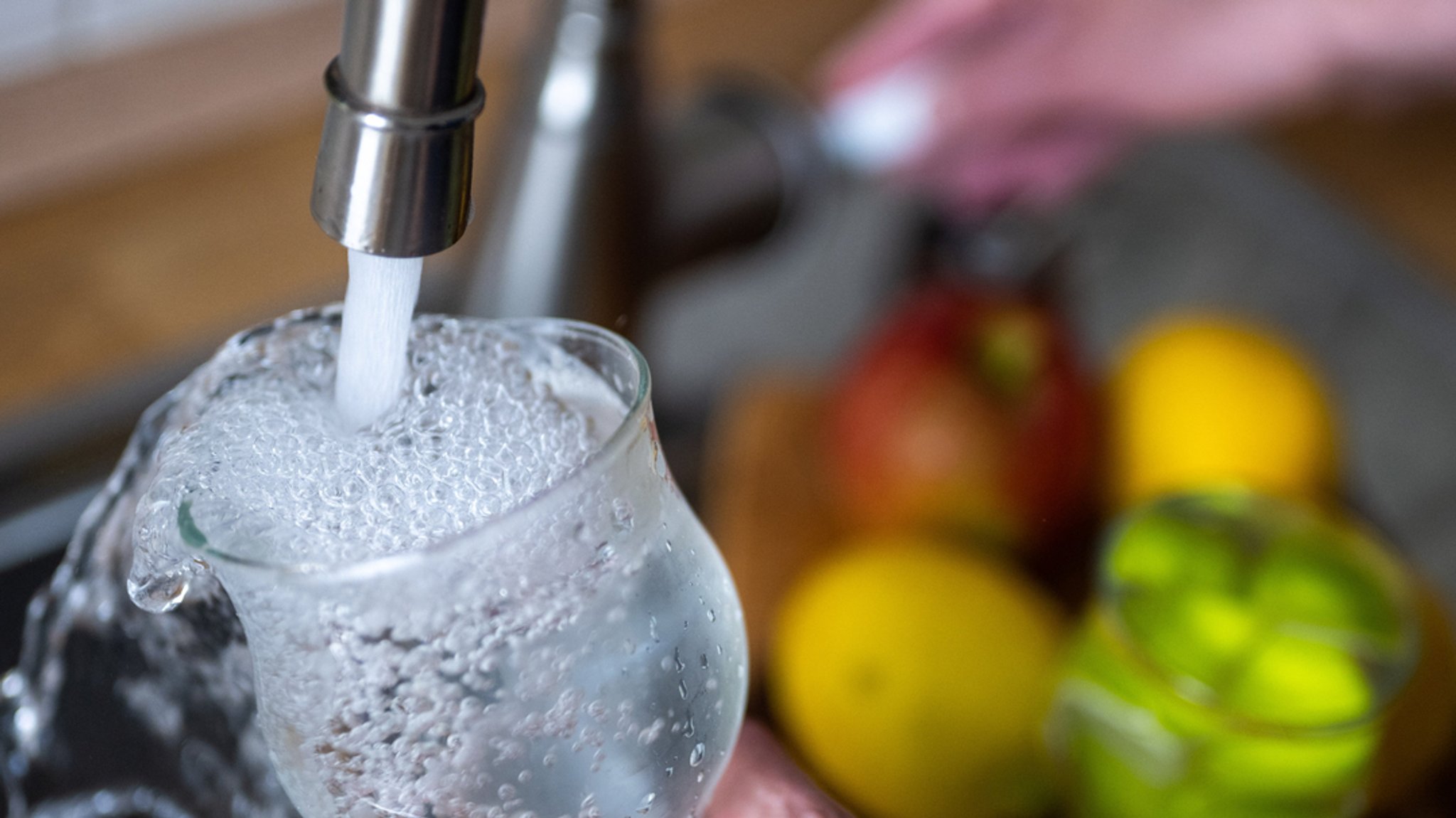 Tinkwasser läuft aus dem Wasserhahn in einer Küche in ein Glas. 