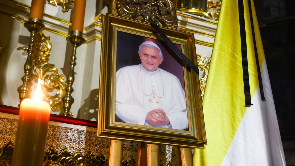 Ein Foto des verstorbenen Papstes Benedikt XVI. mit Trauerflor auf einer Staffelei mit Kerze im Vordergrund.