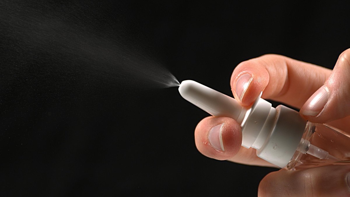 Hand einer Frau und Nasenspray vor schwarzem Hintergrund; Corona-Nasenspray: Nasaler Impfstoff stoppt Übertragung