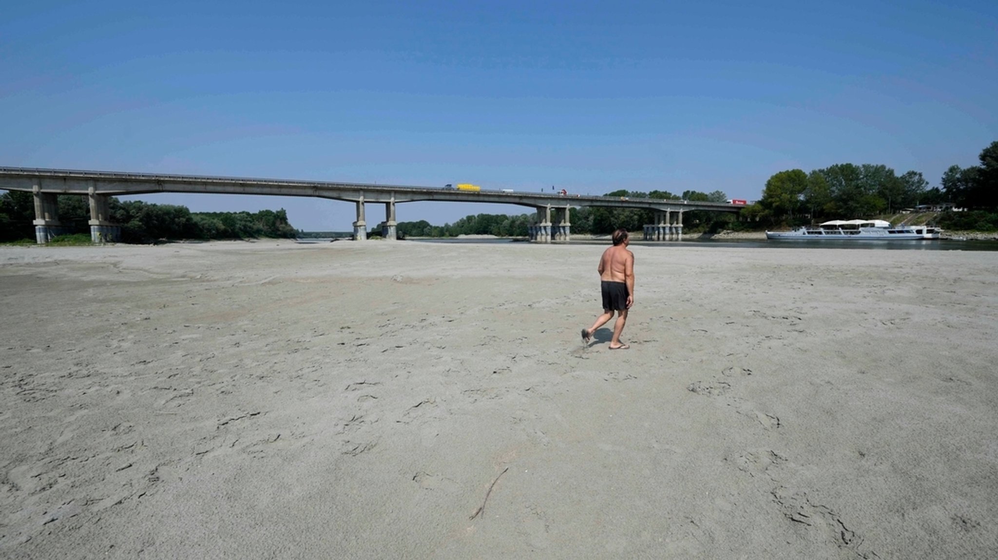 15.06.2022, Italien, Boretto: Ein Mann geht in der Nähe einer Brücke in Boretto, im ausgetrockneten Flussbett des Po spazieren.