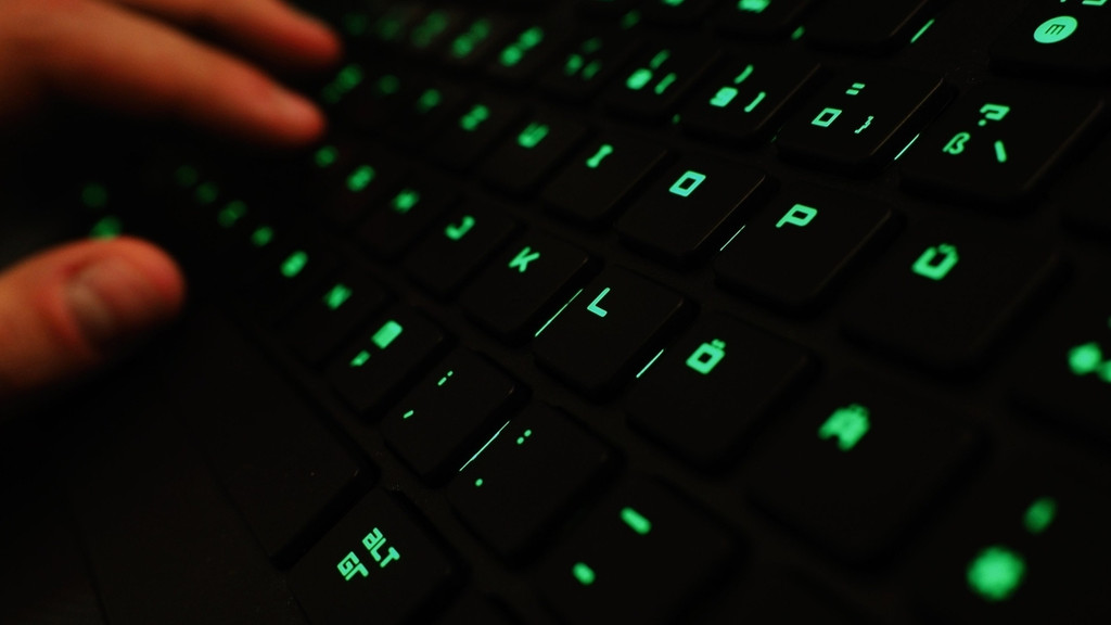 Ein Mann tippt auf einer beleuchteten Tastatur an einem Computer