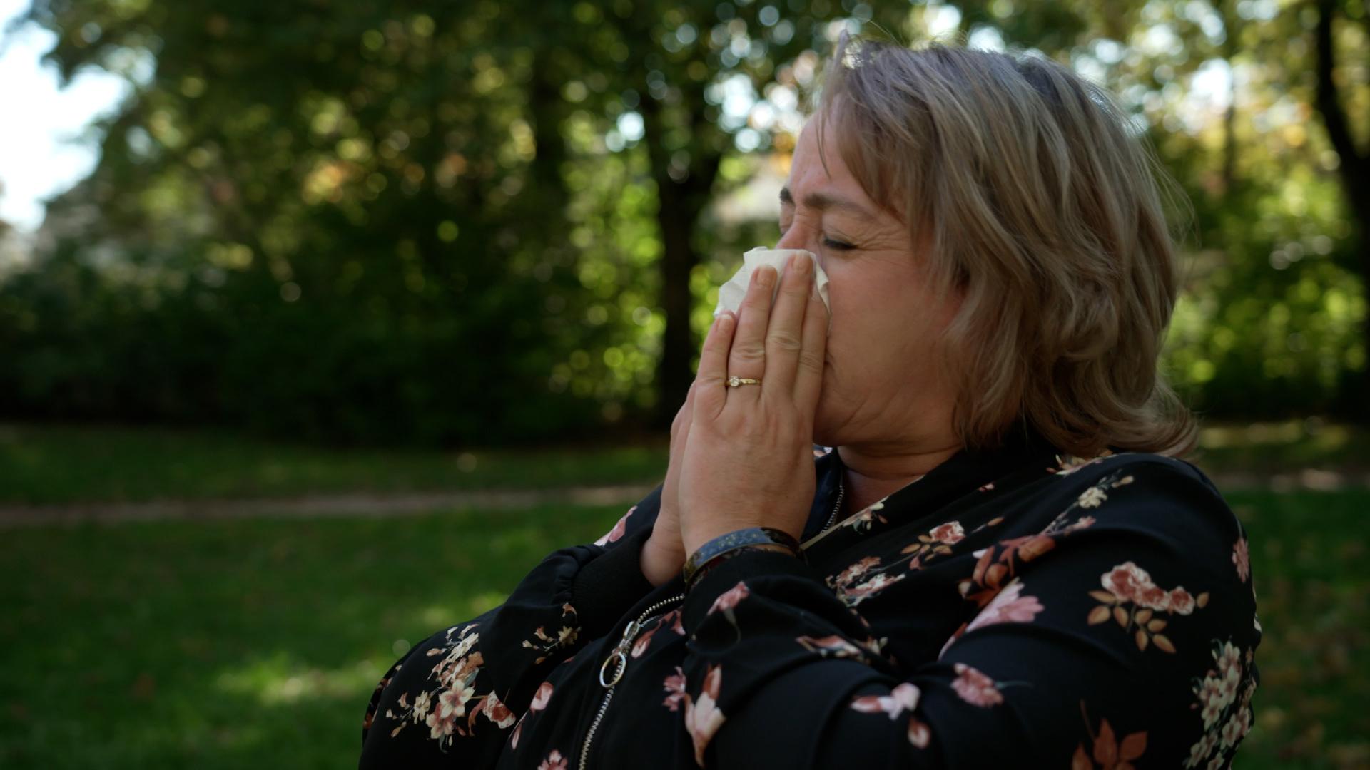 Frau sitzt im Freien und niest in ein Taschentuch