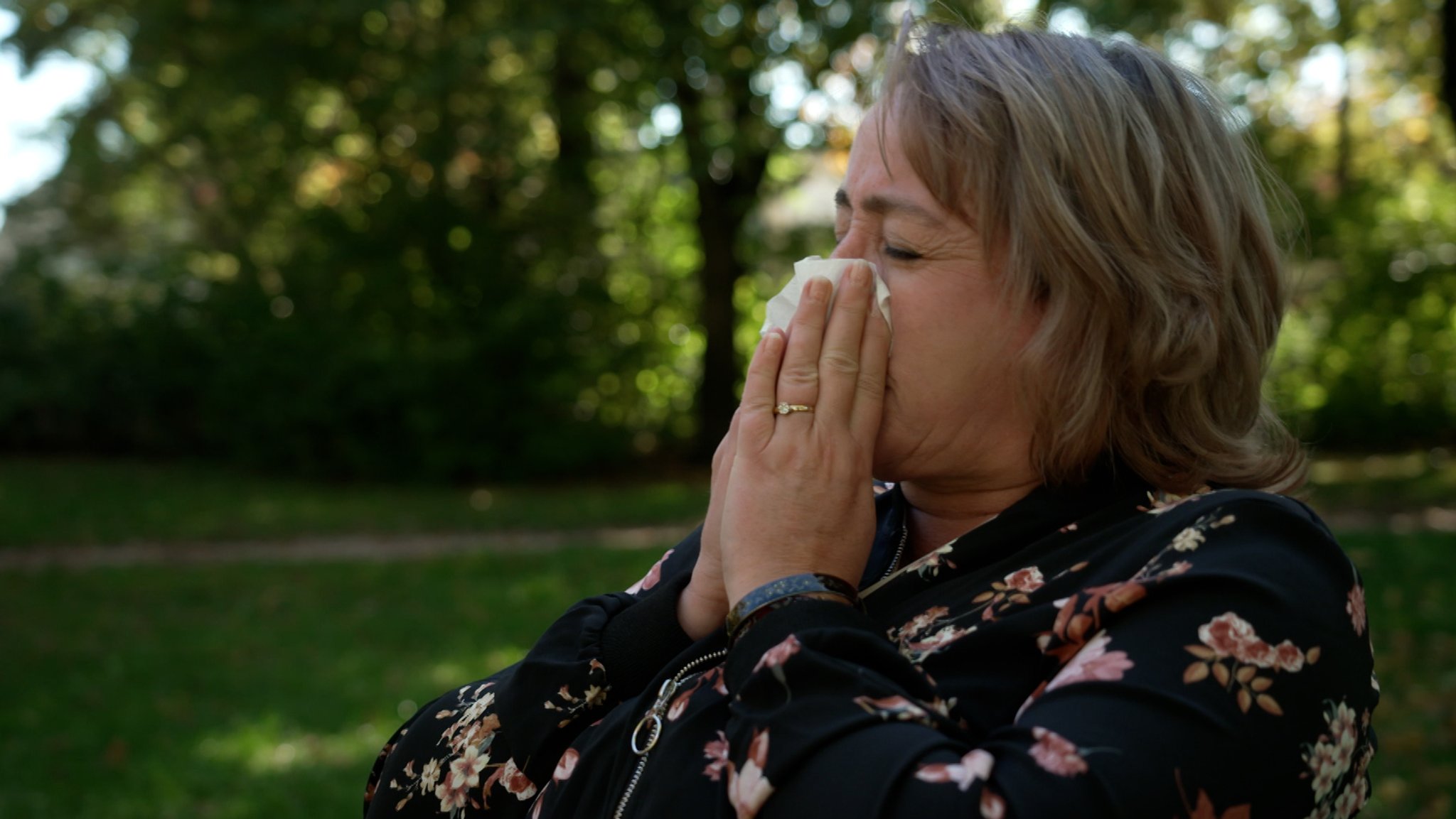 Woman sitting outdoors and sneezing into tissue