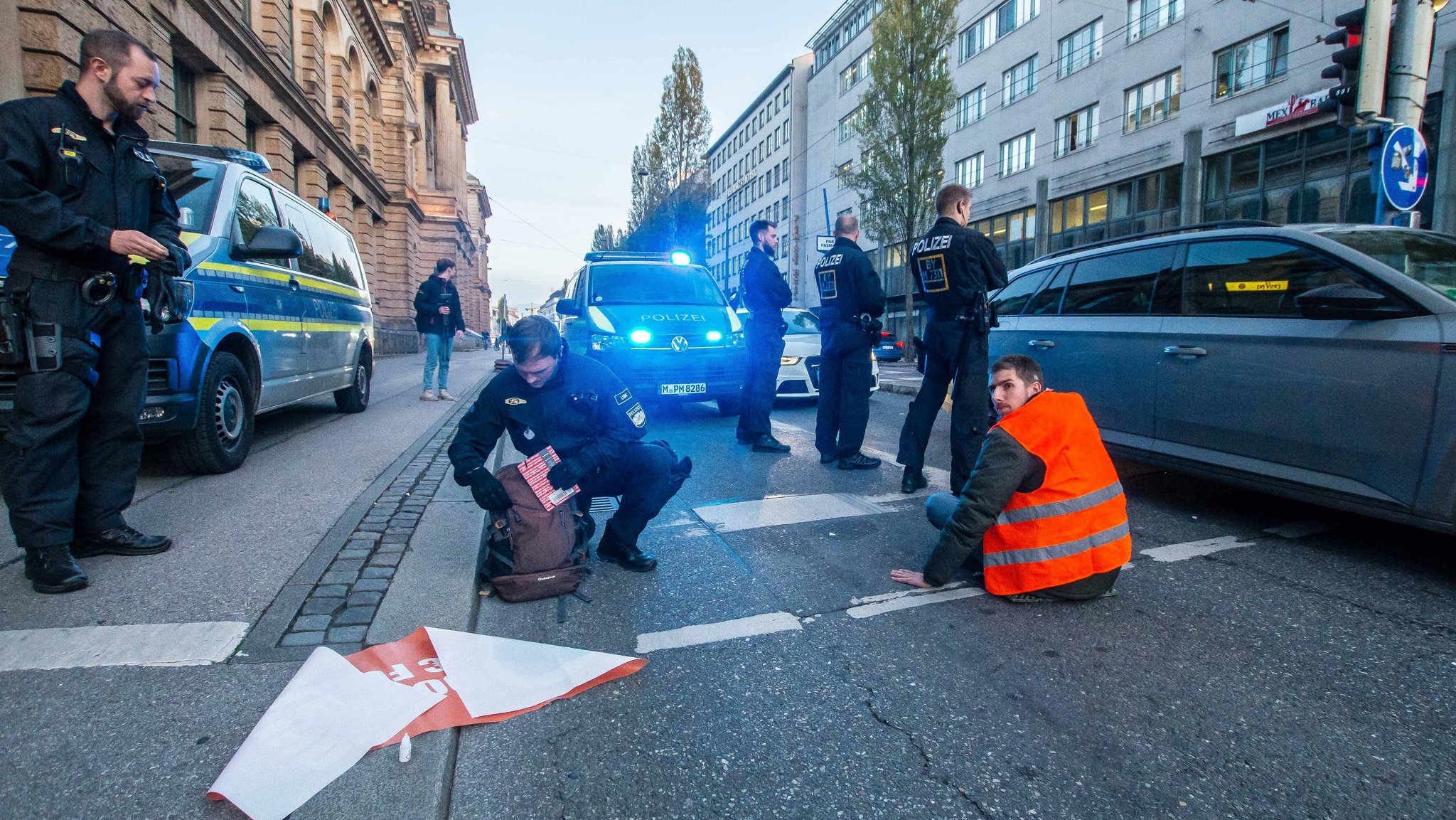 07.11.22: Ein mit der Hand auf der Straße festgeklebter Klima-Aktivist, umgeben von Polizisten.